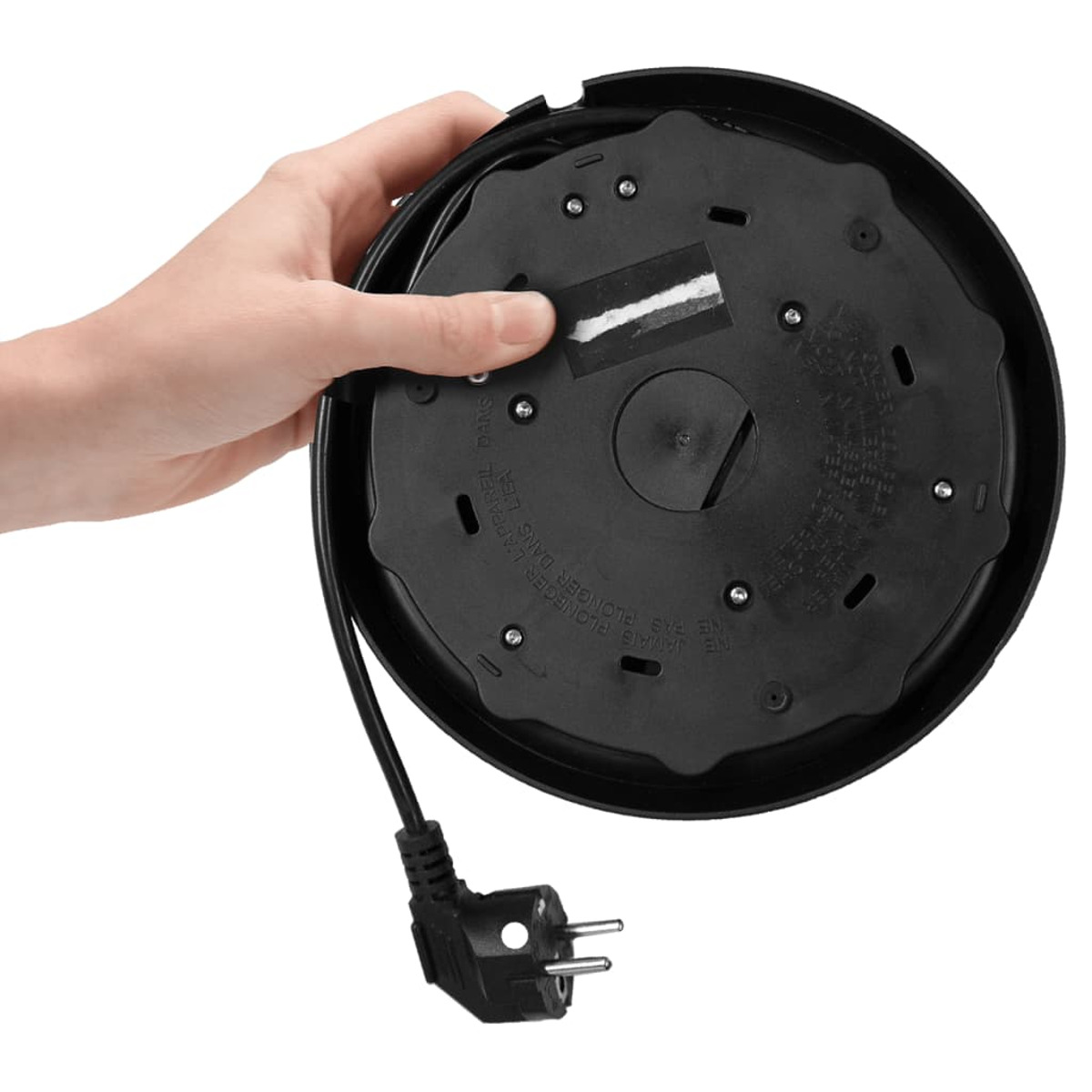 Una mano tiene una base di bollitore nera con cavo di alimentazione e spina. La base è rotonda con testo e viti visibili.