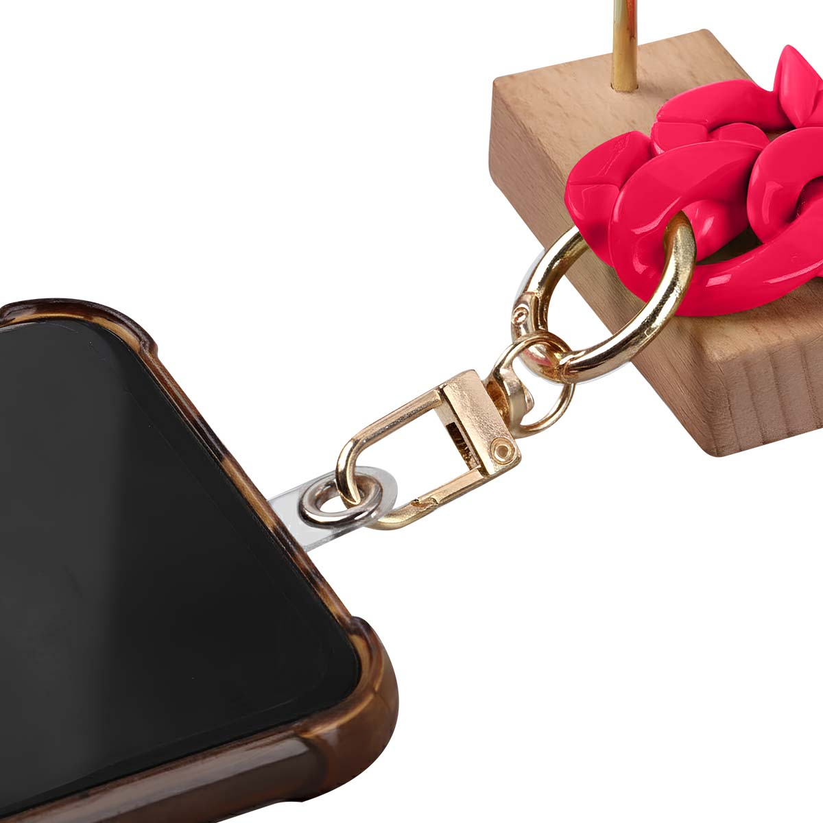 Una custodia per telefono è collegata a una catena rosa e a un fermaglio dorato. La catena è attaccata a un blocco di legno. Sfondo bianco.