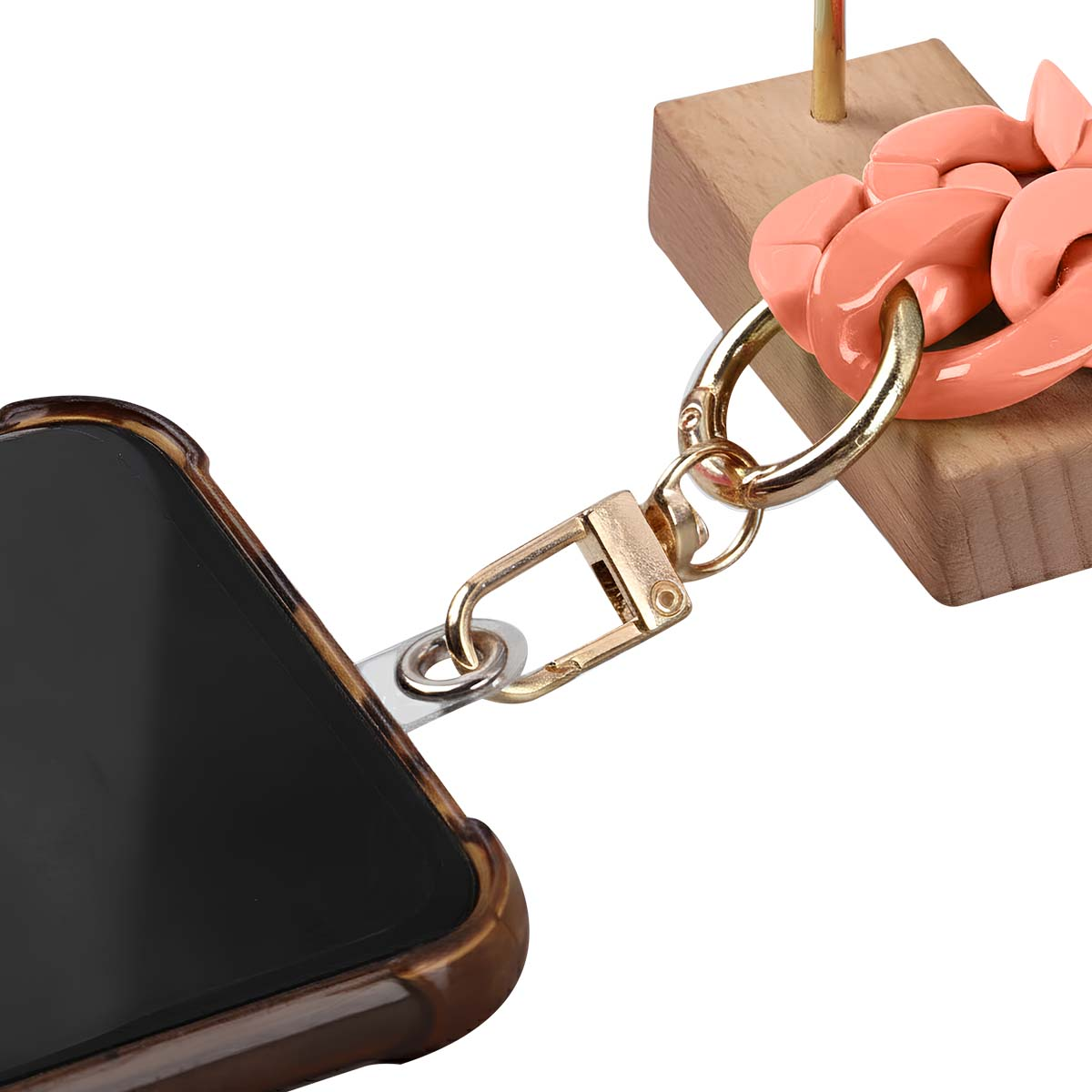 Un telefono in una custodia tartarugata è attaccato a una catena e un fermaglio dorati. Una catena rosa è collegata a un blocco di legno.