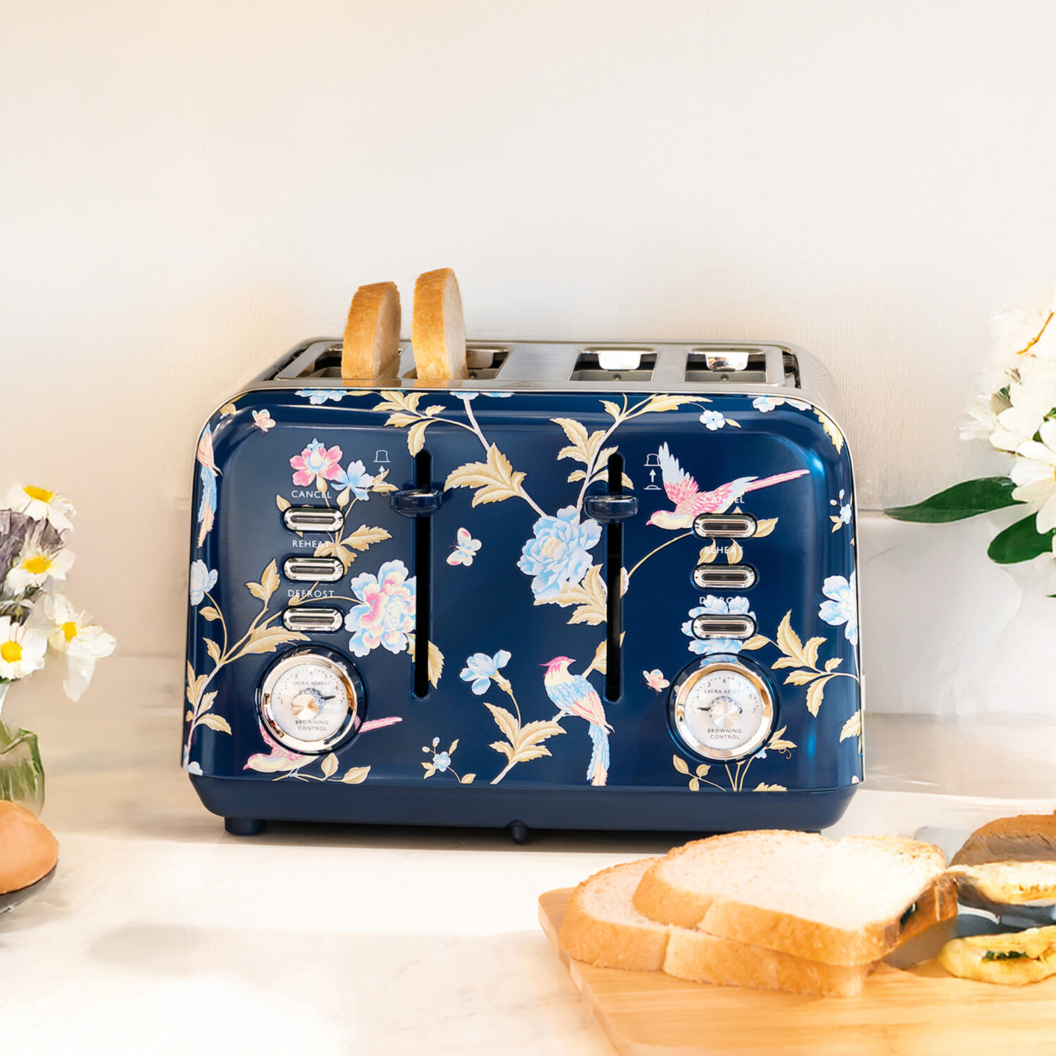 Ein marineblauer, floraler Toaster mit zwei gerösteten Brotscheiben. Brotscheiben und Blumen befinden sich im Vorder- und Hintergrund.