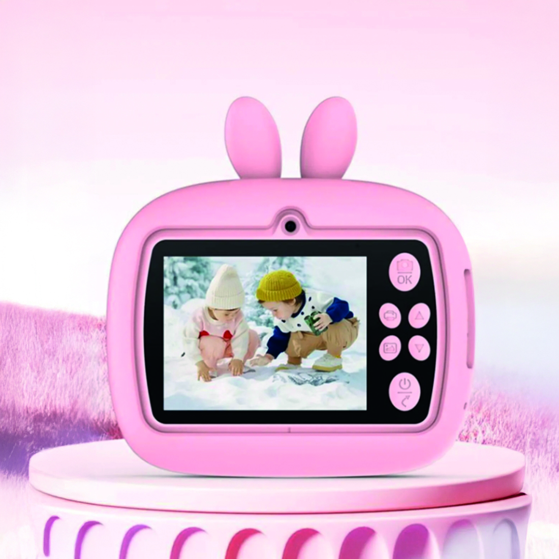 Pembe tavşan kulaklı kamera, karda oynayan iki çocuğu gösteriyor. Kamera, bulanık pembe bir arka plan üzerinde pembe bir standın üzerinde.