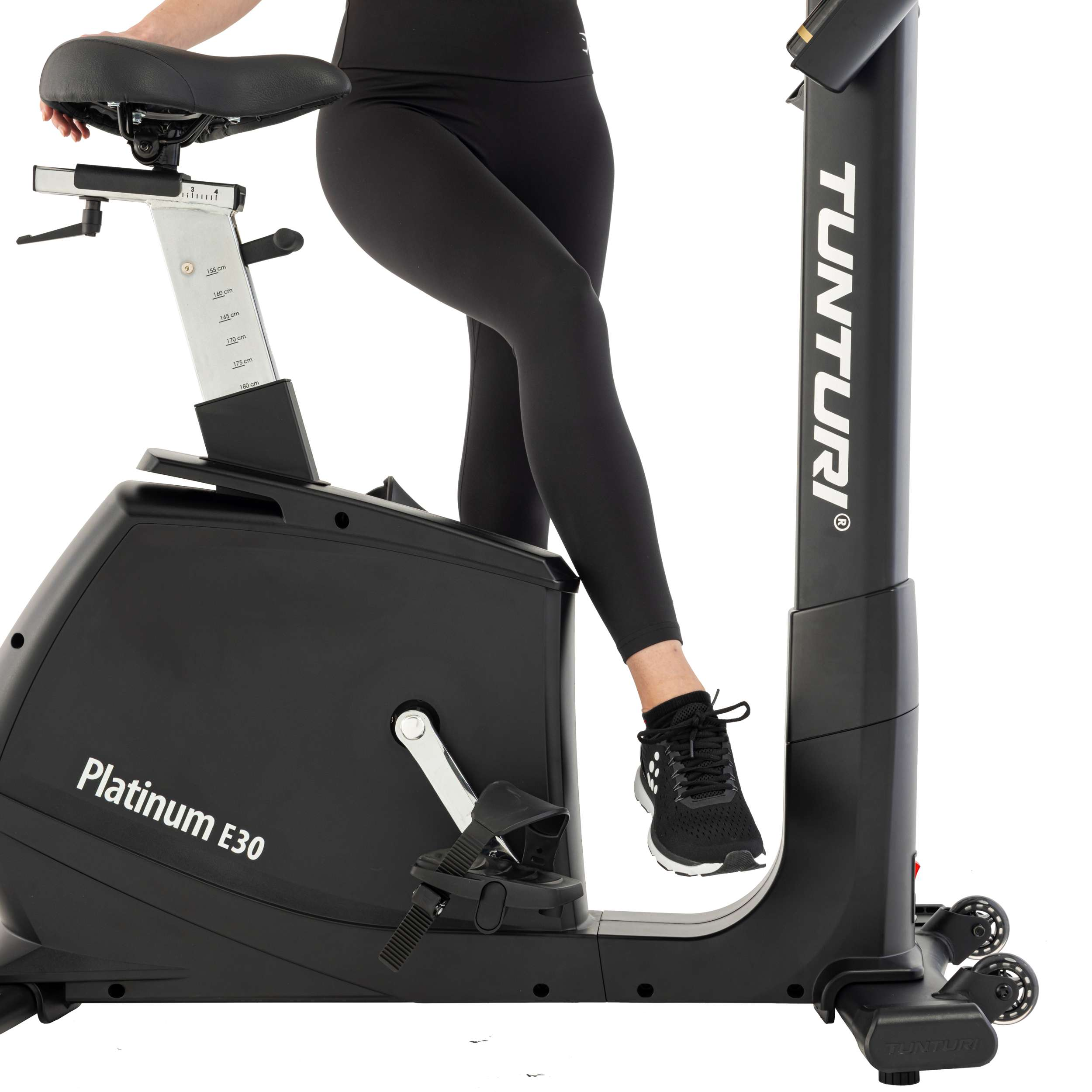 Een persoon zit op een zwarte hometrainer. De fiets heeft het merk Tunturi. De persoon draagt ​​een zwarte legging en schoenen.