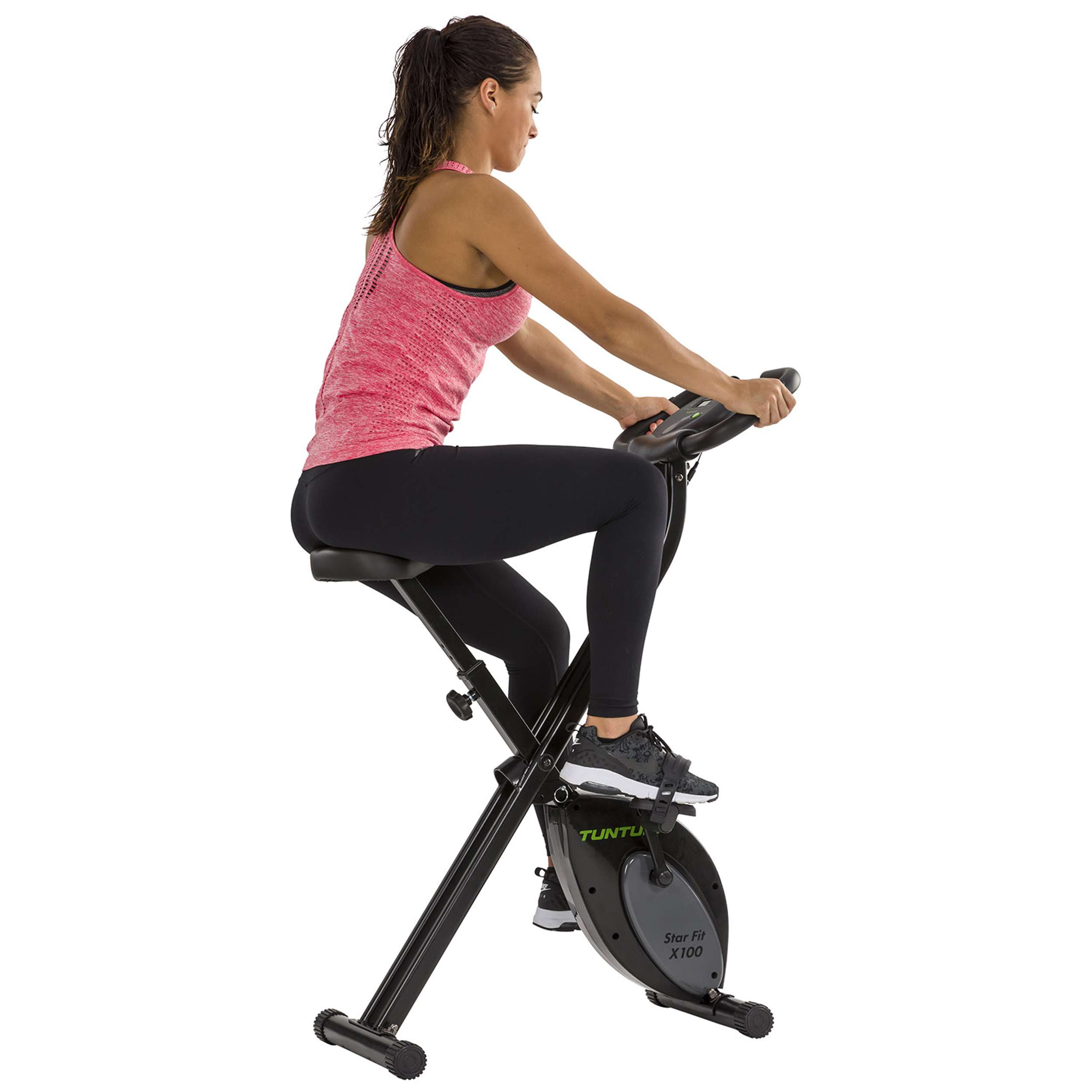 Een vrouw sport op een hometrainer. Ze draagt een roze top en een zwarte legging. De fiets is zwart.