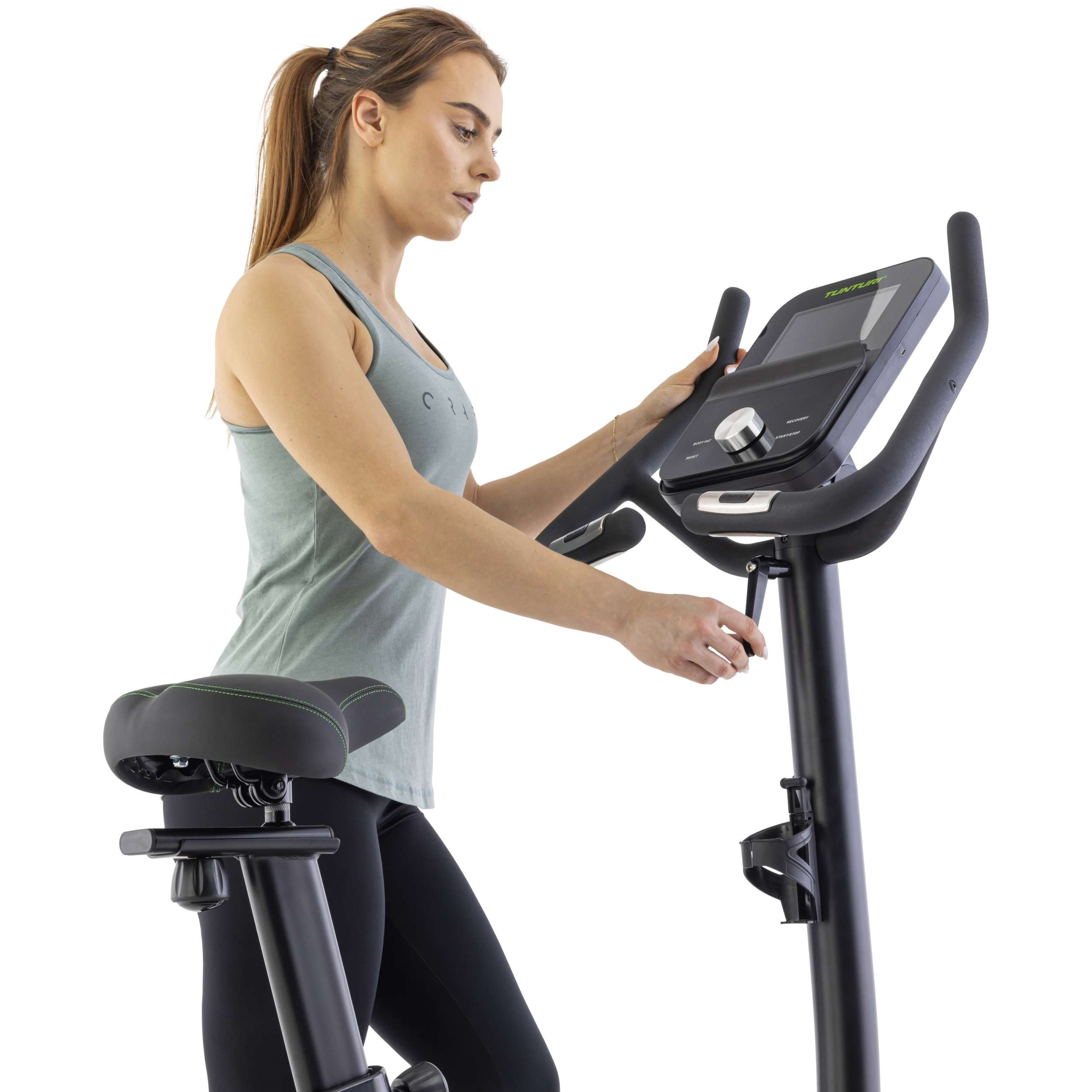 Vrouw op hometrainer past instellingen aan. Fiets is zwart, vrouw draagt grijze top en zwarte broek.