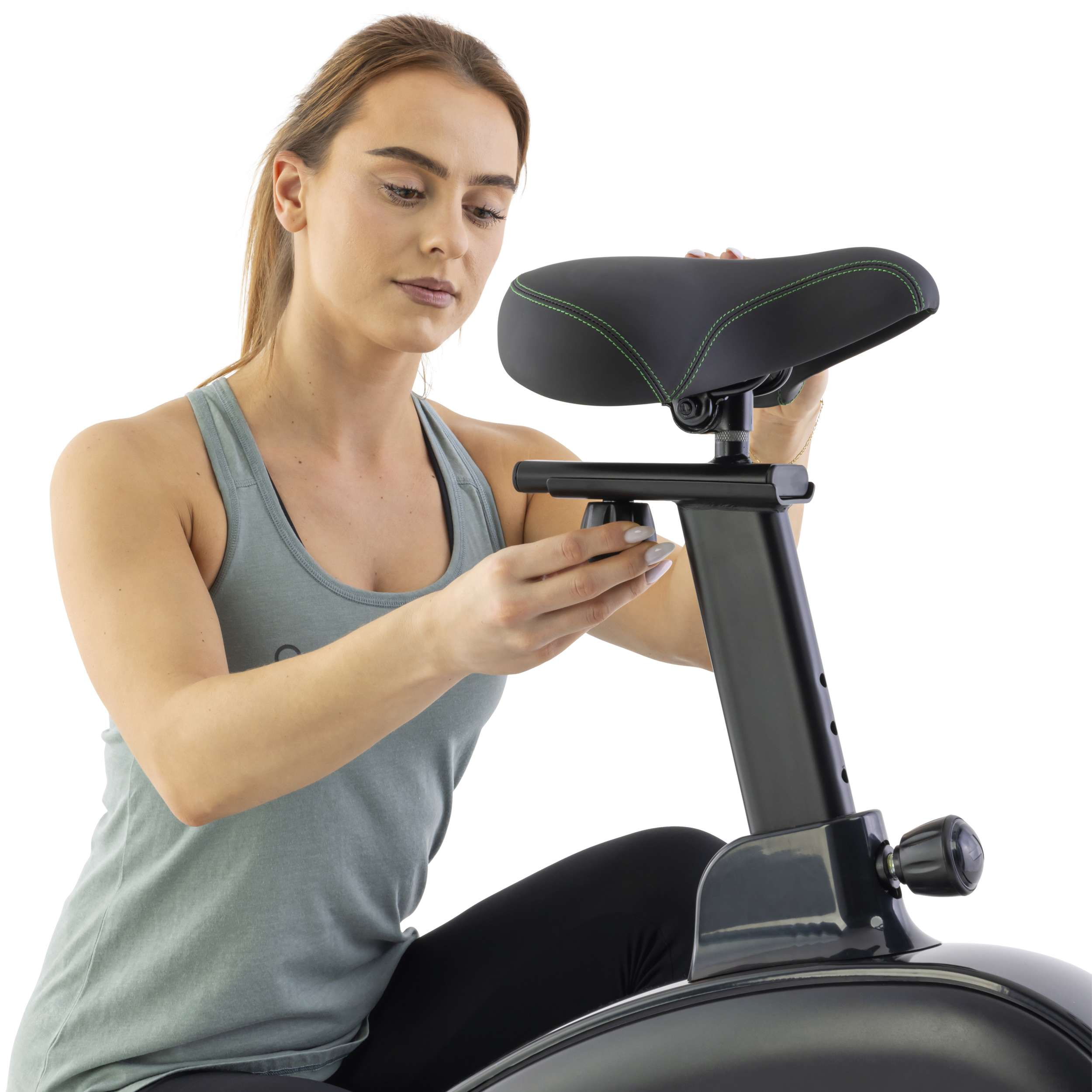Een vrouw verstelt de zitting van een hometrainer. Ze draagt een grijze tanktop en zwarte leggings. De fiets is zwart.