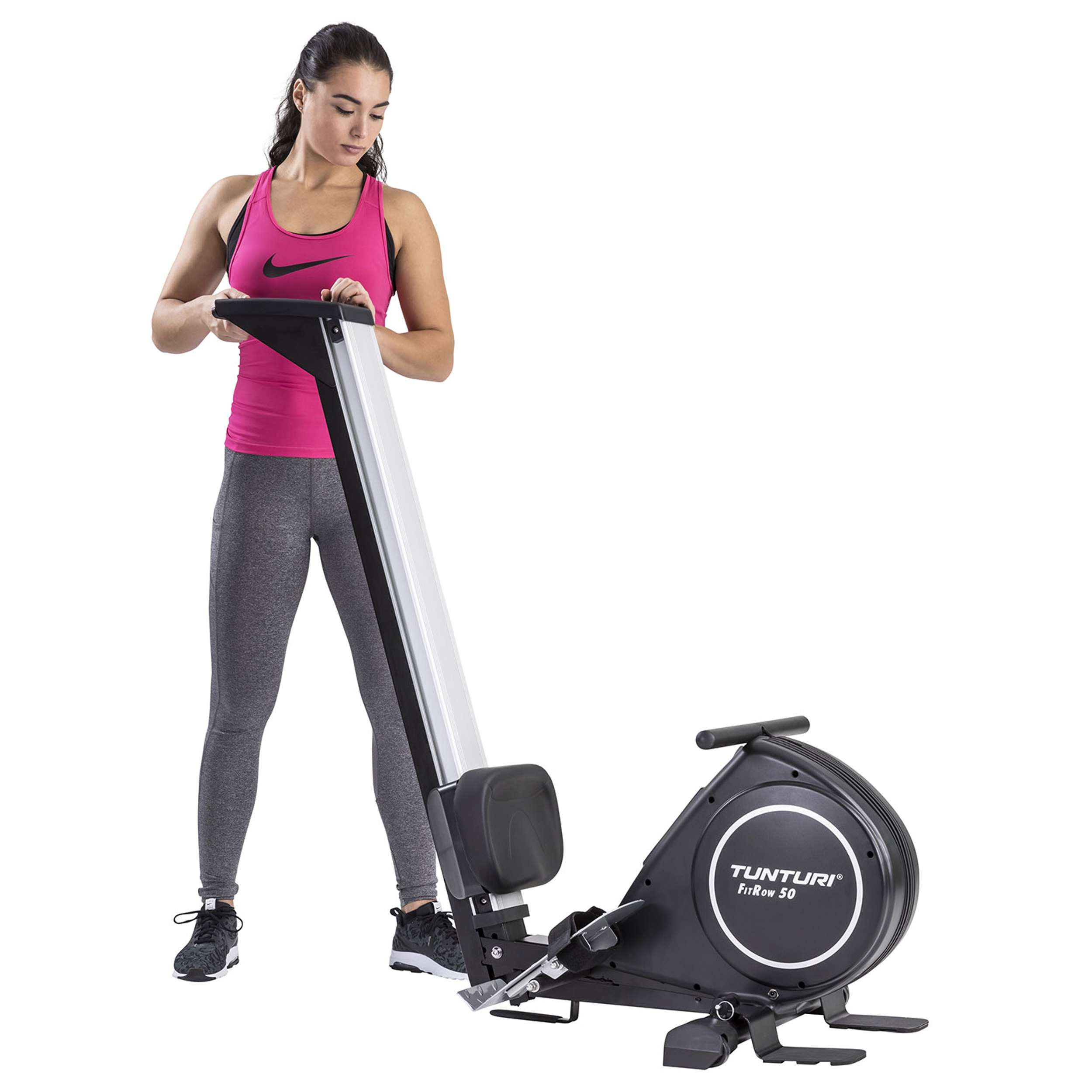 Een vrouw in roze top, grijze legging en zwarte schoenen staat bij een roeimachine.