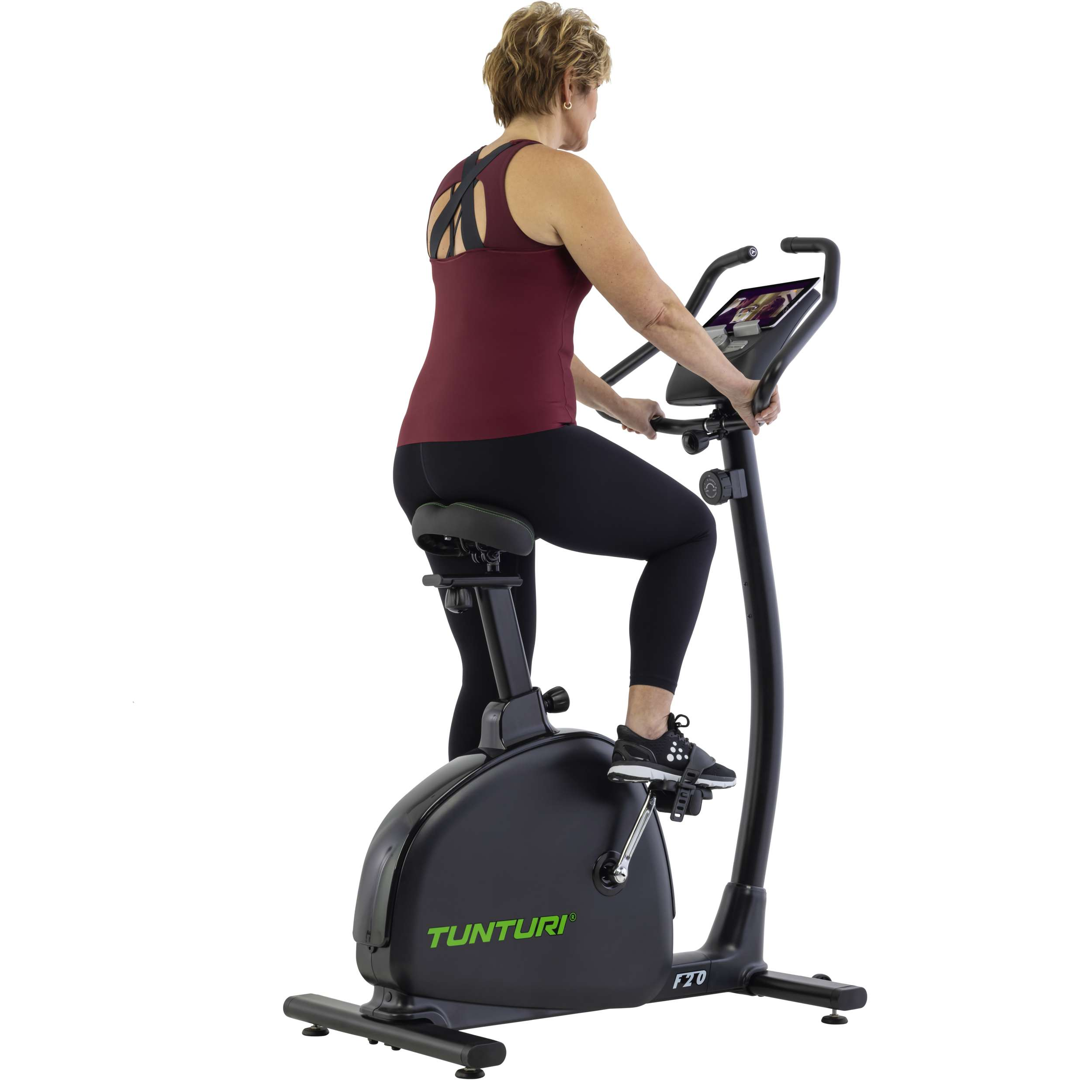Een vrouw sport op een zwarte hometrainer. Ze draagt een bordeauxrode top en zwarte leggings.