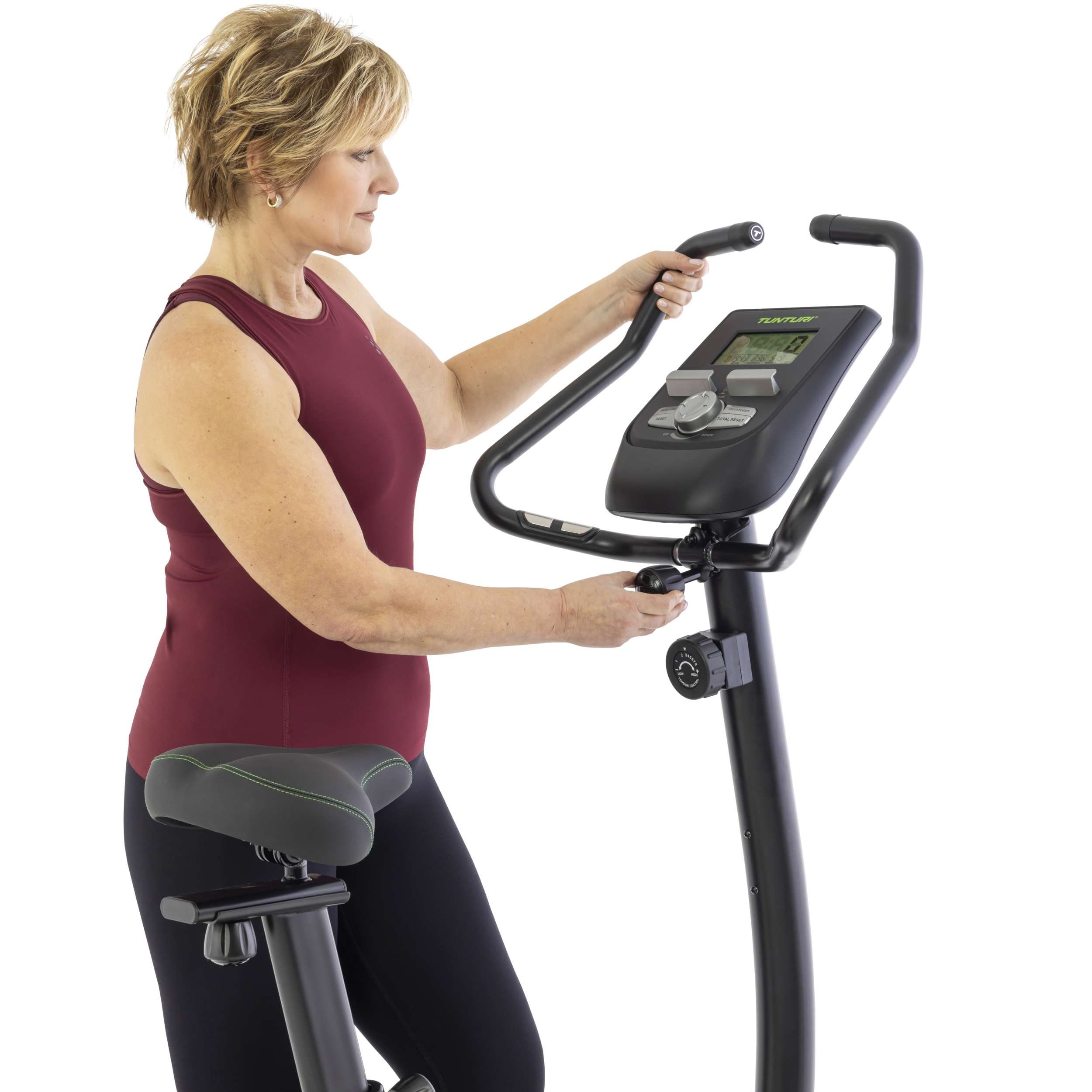 Vrouw in bordeauxrode top op hometrainer. Ze past de instellingen aan. Zwarte fiets op witte achtergrond.