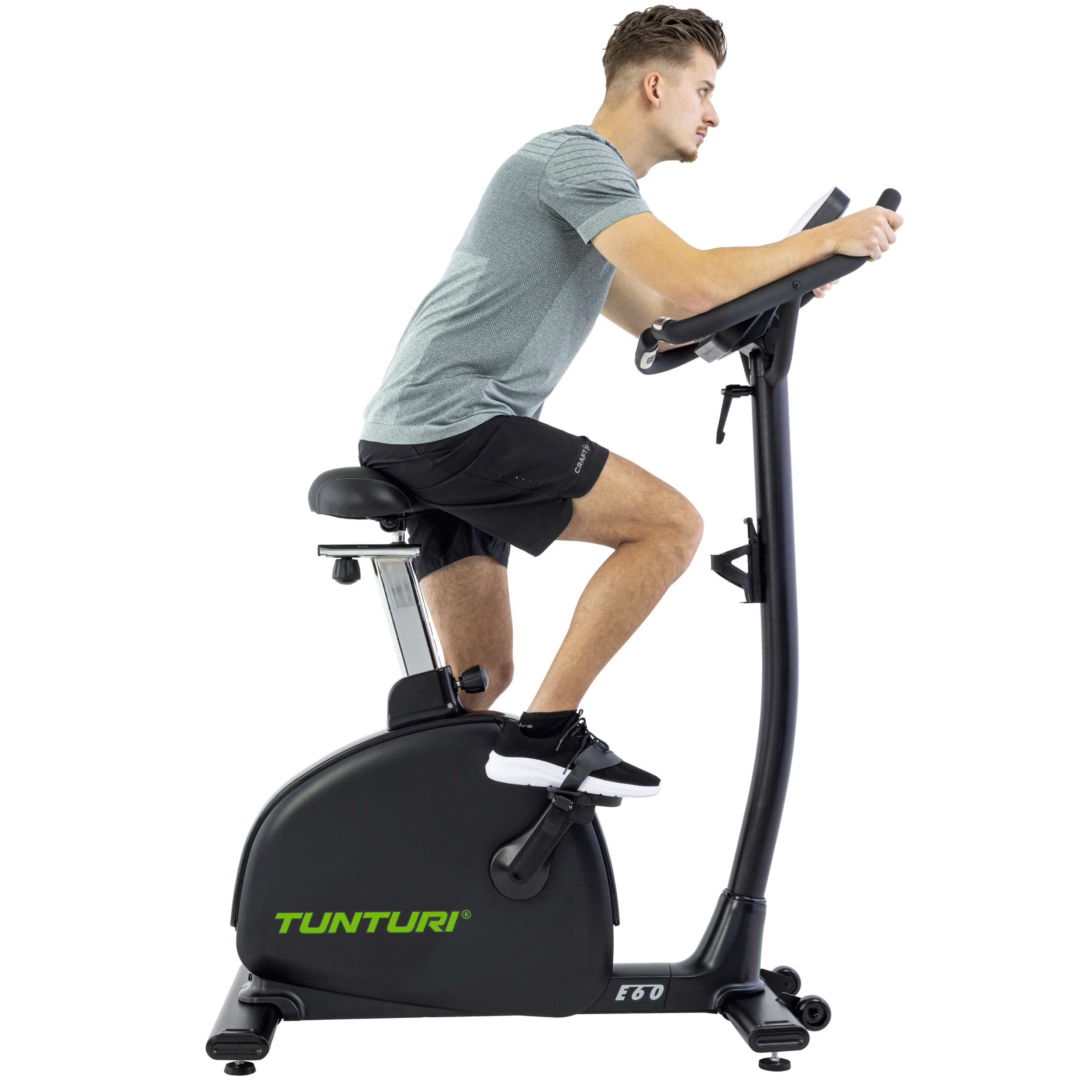 Een man in een grijs shirt en zwarte korte broek fietst op een zwarte hometrainer tegen een witte achtergrond.