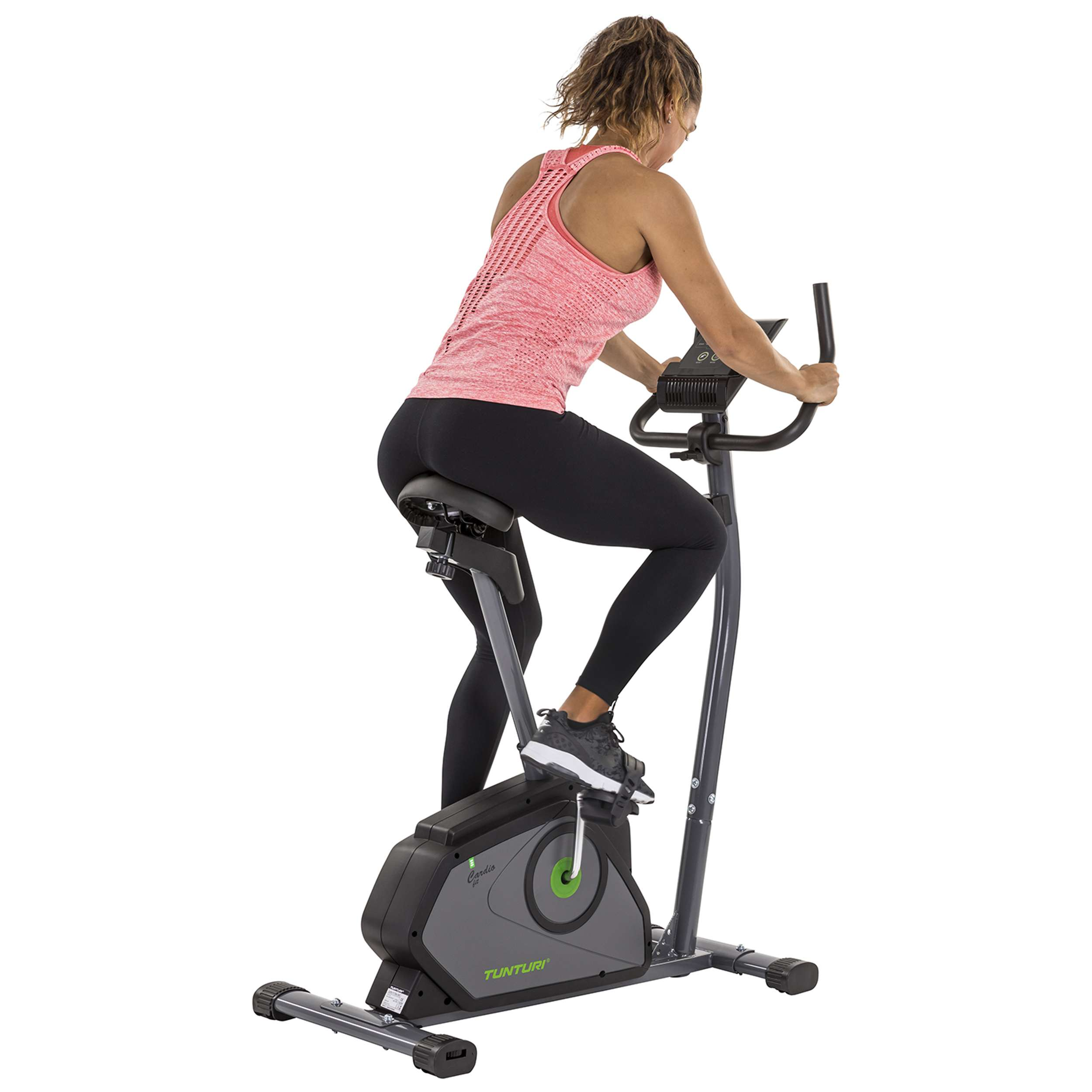 Vrouw op hometrainer. Ze draagt een roze top en zwarte legging. De fiets is grijs met groene accenten.