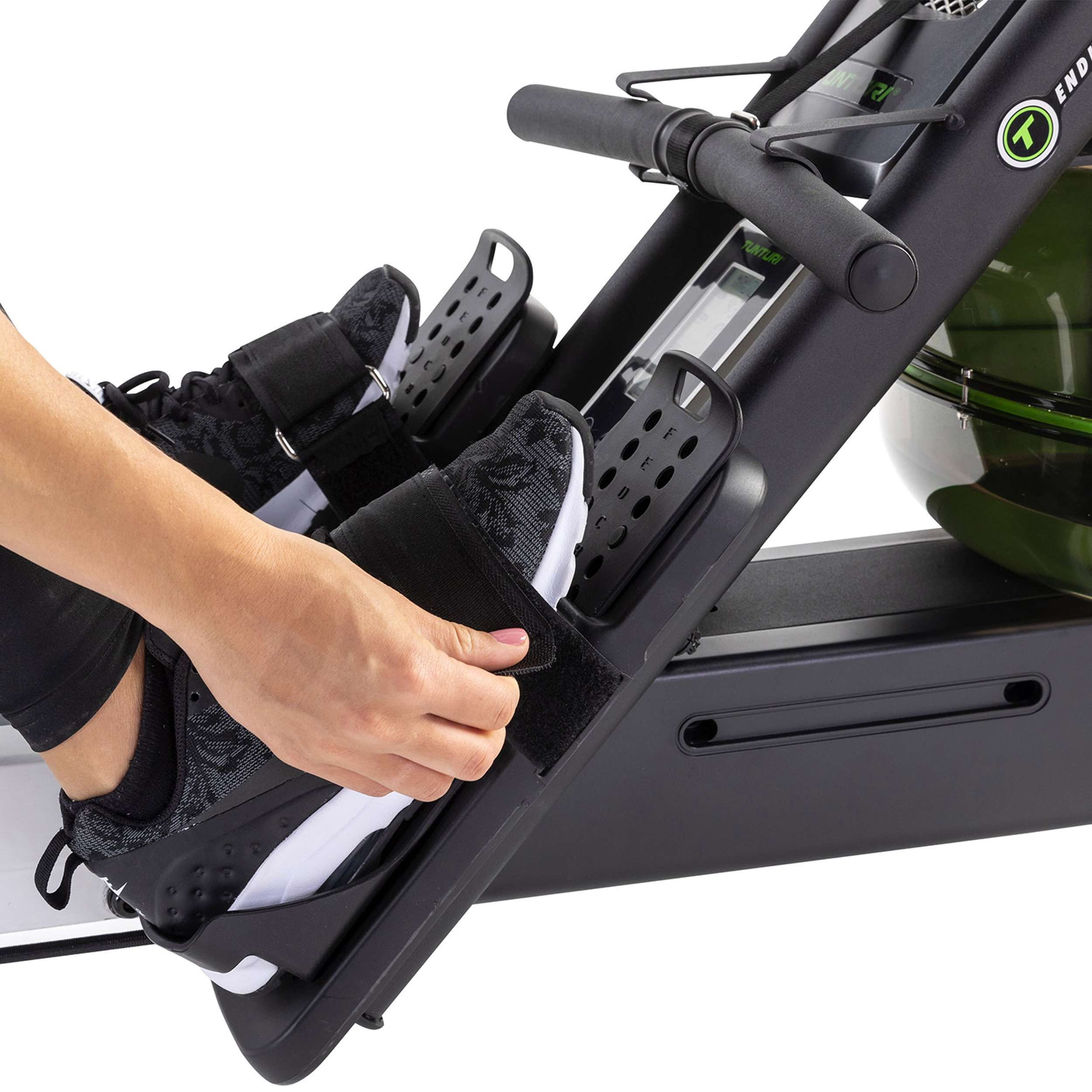 De voeten van een persoon in sportschoenen zijn vastgemaakt aan een roeimachine. Een hand verstelt de riem.