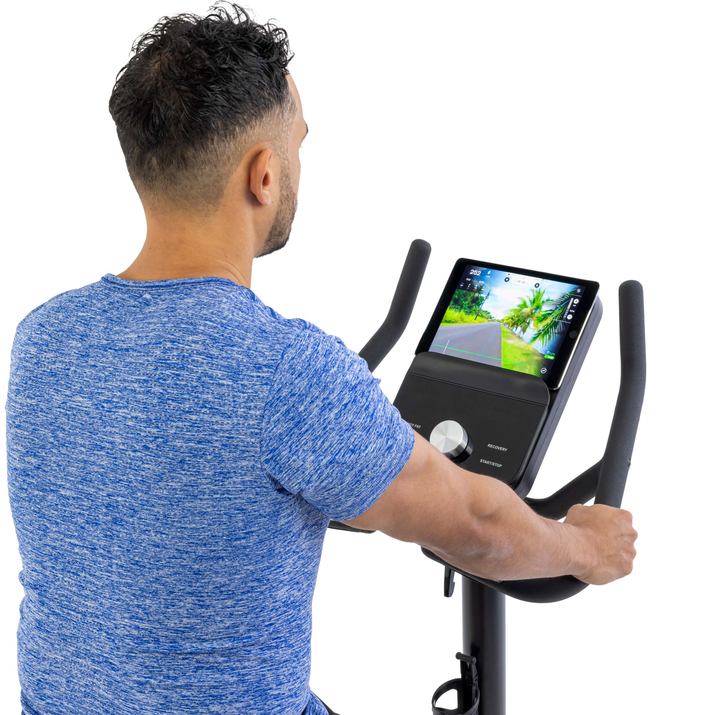 Man op hometrainer, wegkijkend. Hij draagt blauw, kijkt naar het scherm. De fiets heeft zwarte handvatten en een scherm.