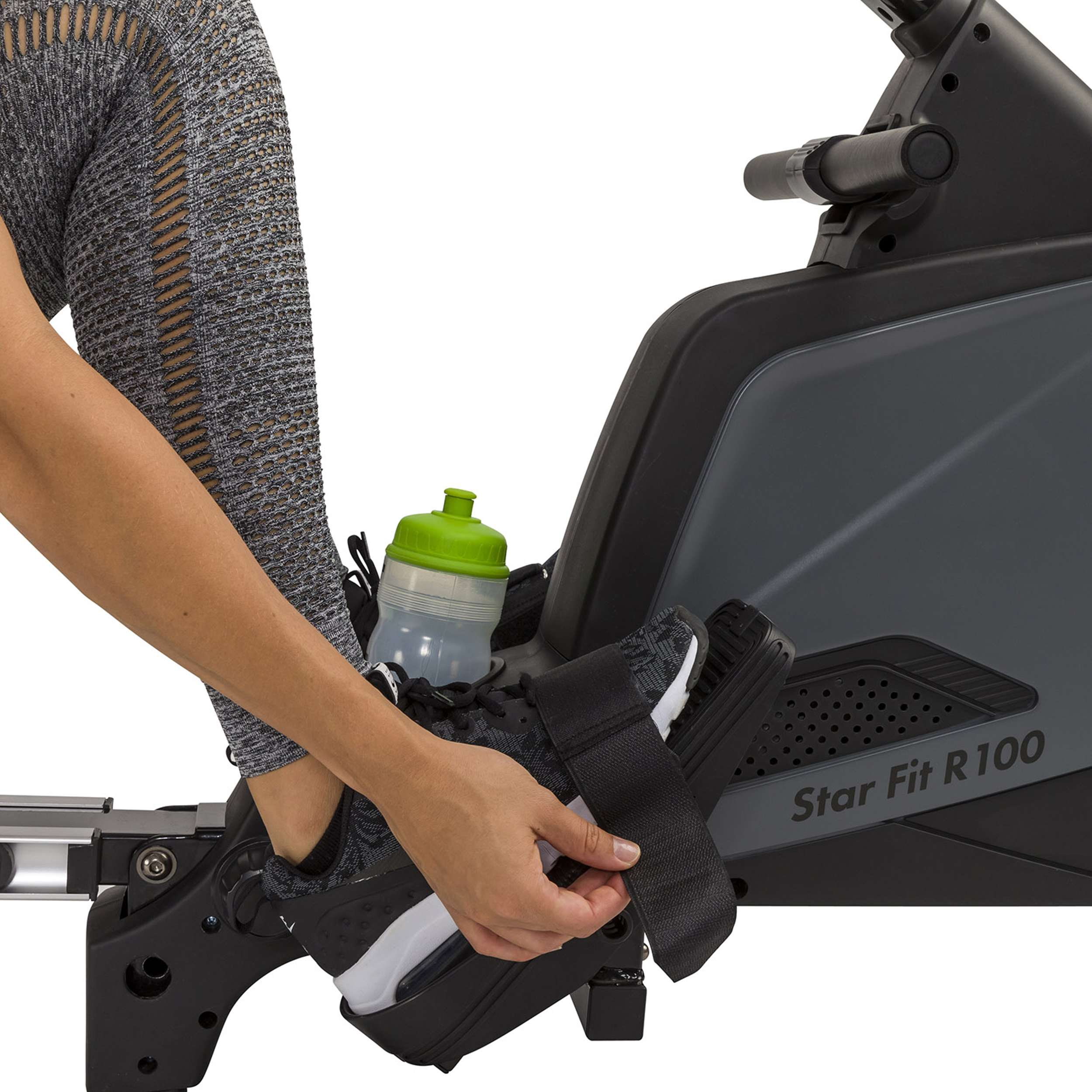 Persoon zet schoen vast op een hometrainer. Grijze legging, zwart-witte schoen, waterfles. Star Fit R 100.