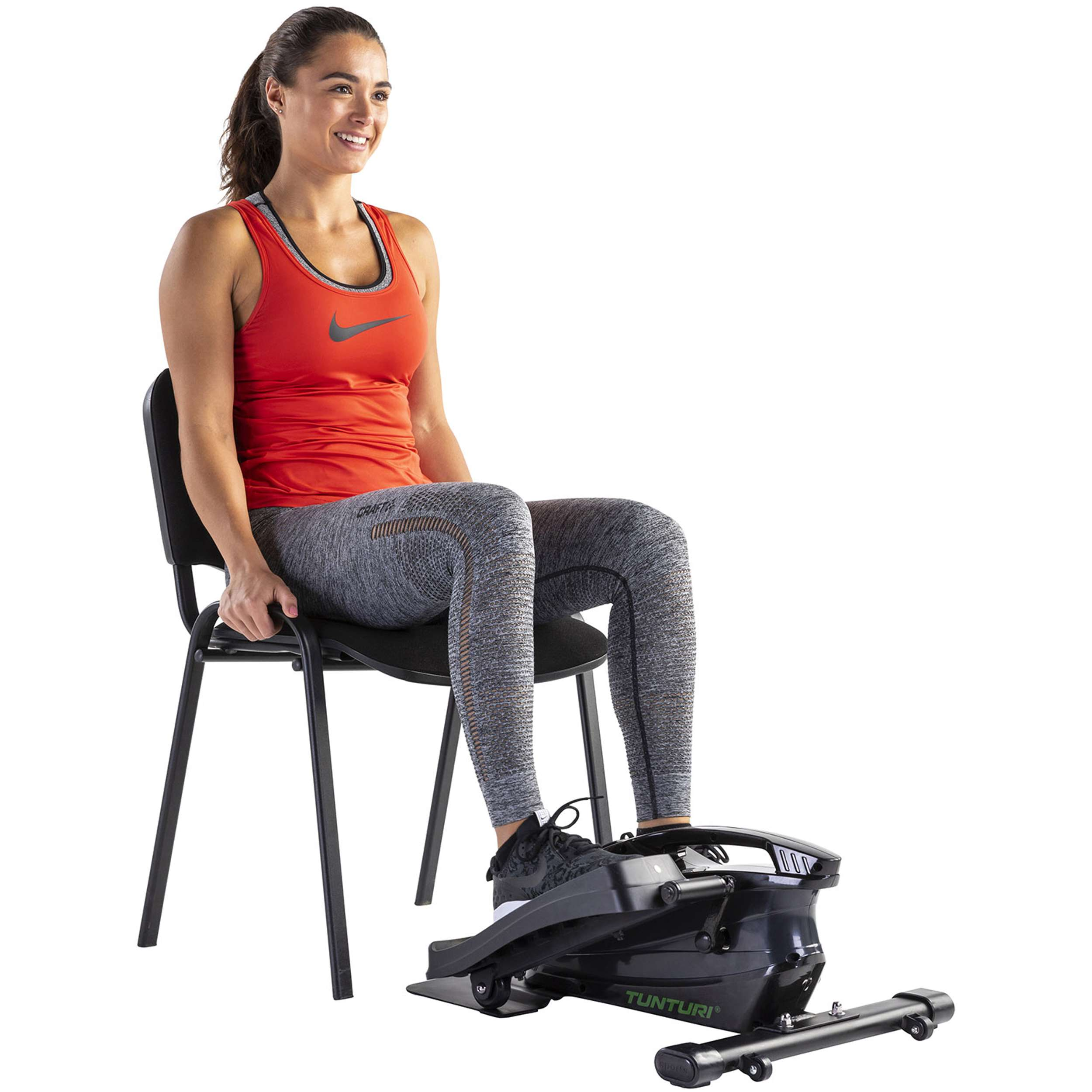 Vrouw in rode top traint op een steptrainer. Ze zit op een stoel. Zwarte machine en schoenen zichtbaar.