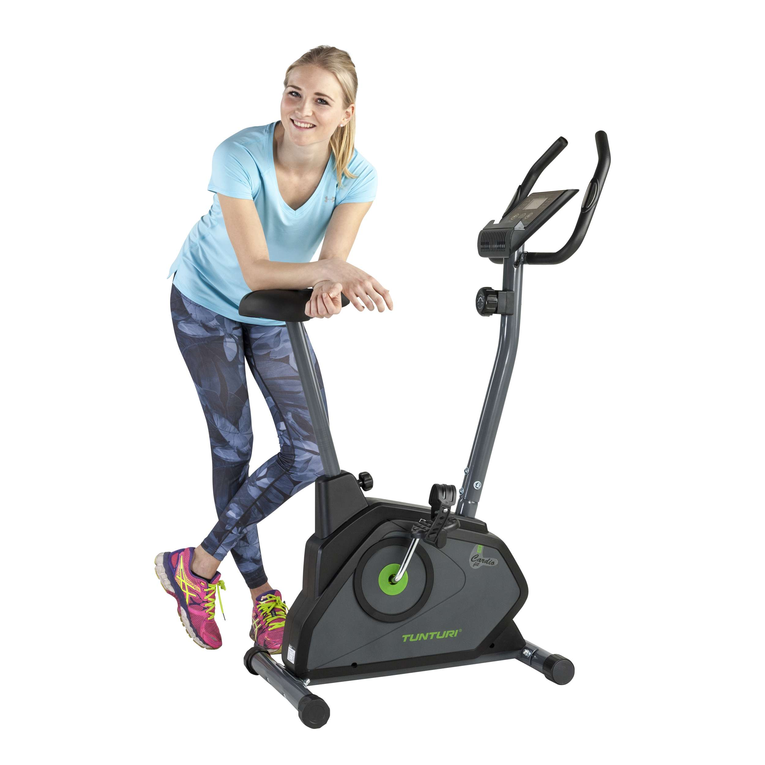 Vrouw in blauw shirt en legging met patroon leunt op een hometrainer. Roze en gele sneakers zijn zichtbaar.