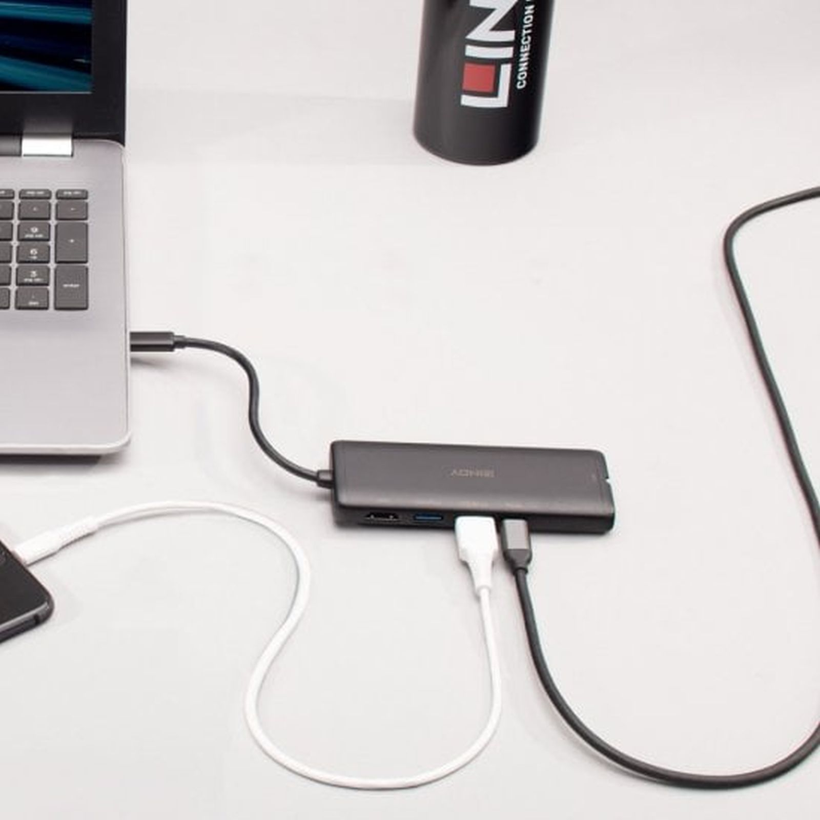 Laptop mit USB-Hub verbunden. Kabel sind mit einem Telefon und einem schwarzen Zylinder mit dem Wort LIN verbunden.
