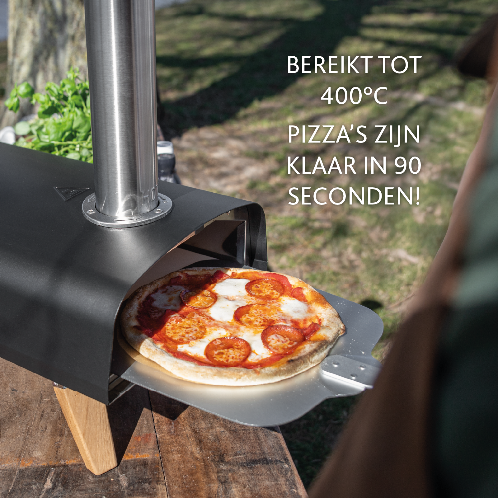 Een pizza in een buitenoven wordt met een metalen spatel verwijderd. De oven is zwart en heet.
