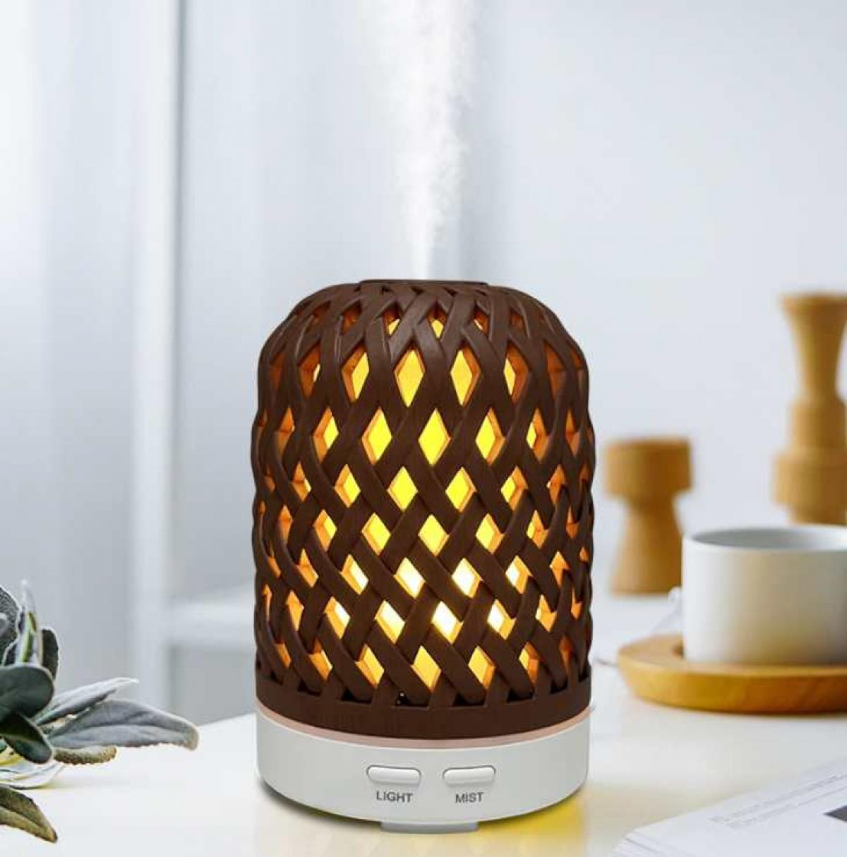 Ein brauner gewebter Diffusor mit gelbem Licht, das aus den Öffnungen austritt. Er steht auf einem weißen Sockel mit 'Light'- und 'Mist'-Tasten.