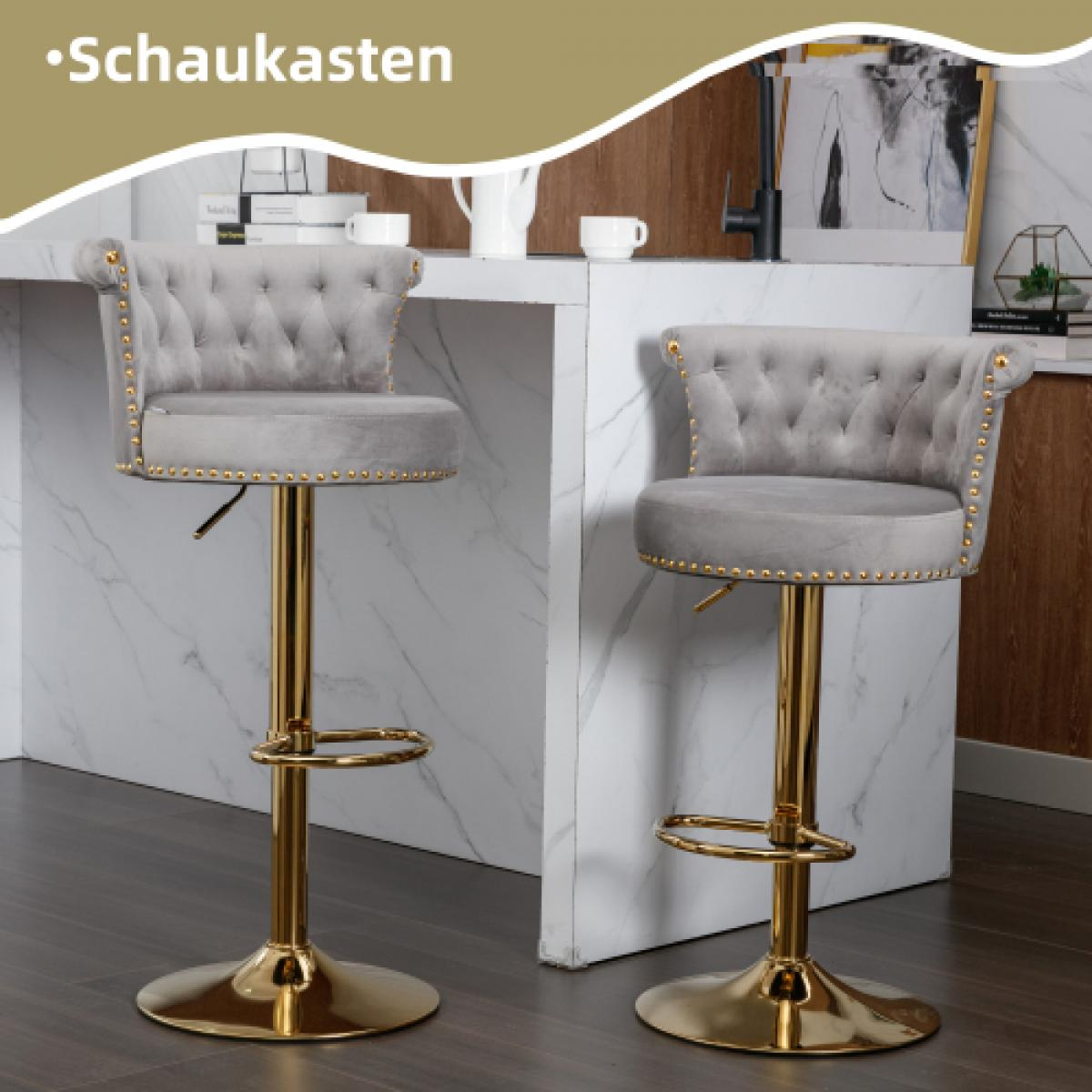 Zwei graue Samt-Barhocker mit goldenen Füßen stehen vor einer weißen Theke. Die Hocker haben knopfgetuftete Rücken und goldene Akzente.