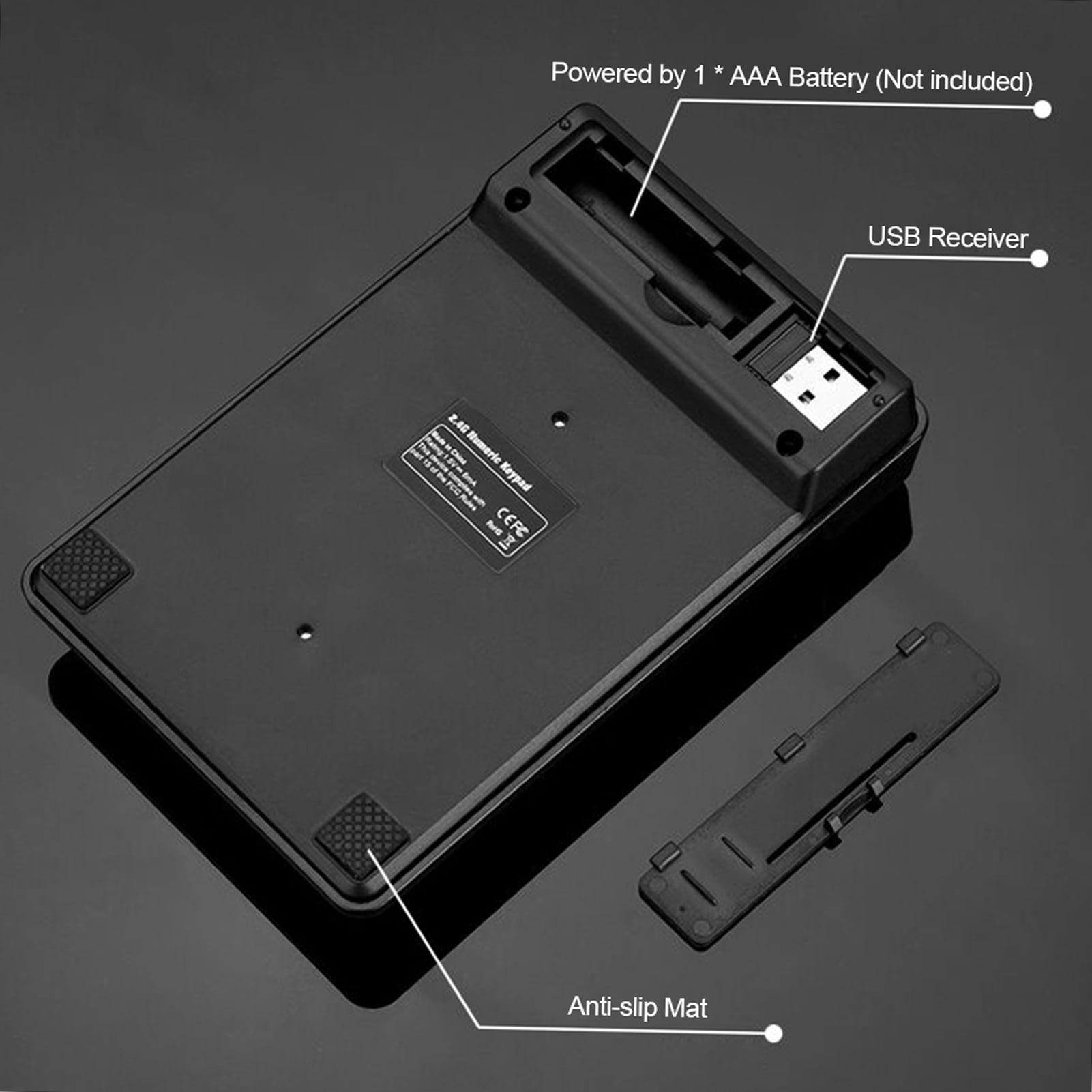 Schwarzes numerisches Keypad mit Batterieschacht, USB-Empfänger und Anti-Rutsch-Matten. Eine Abdeckung liegt daneben.