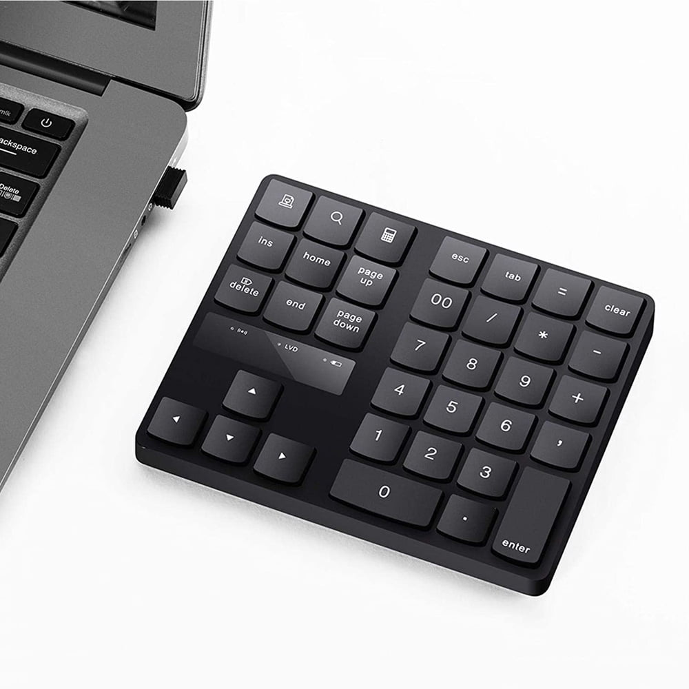 Ein schwarzes Nummernfeld mit weißen Tastenbeschriftungen liegt auf einer weißen Oberfläche neben einem Laptop.