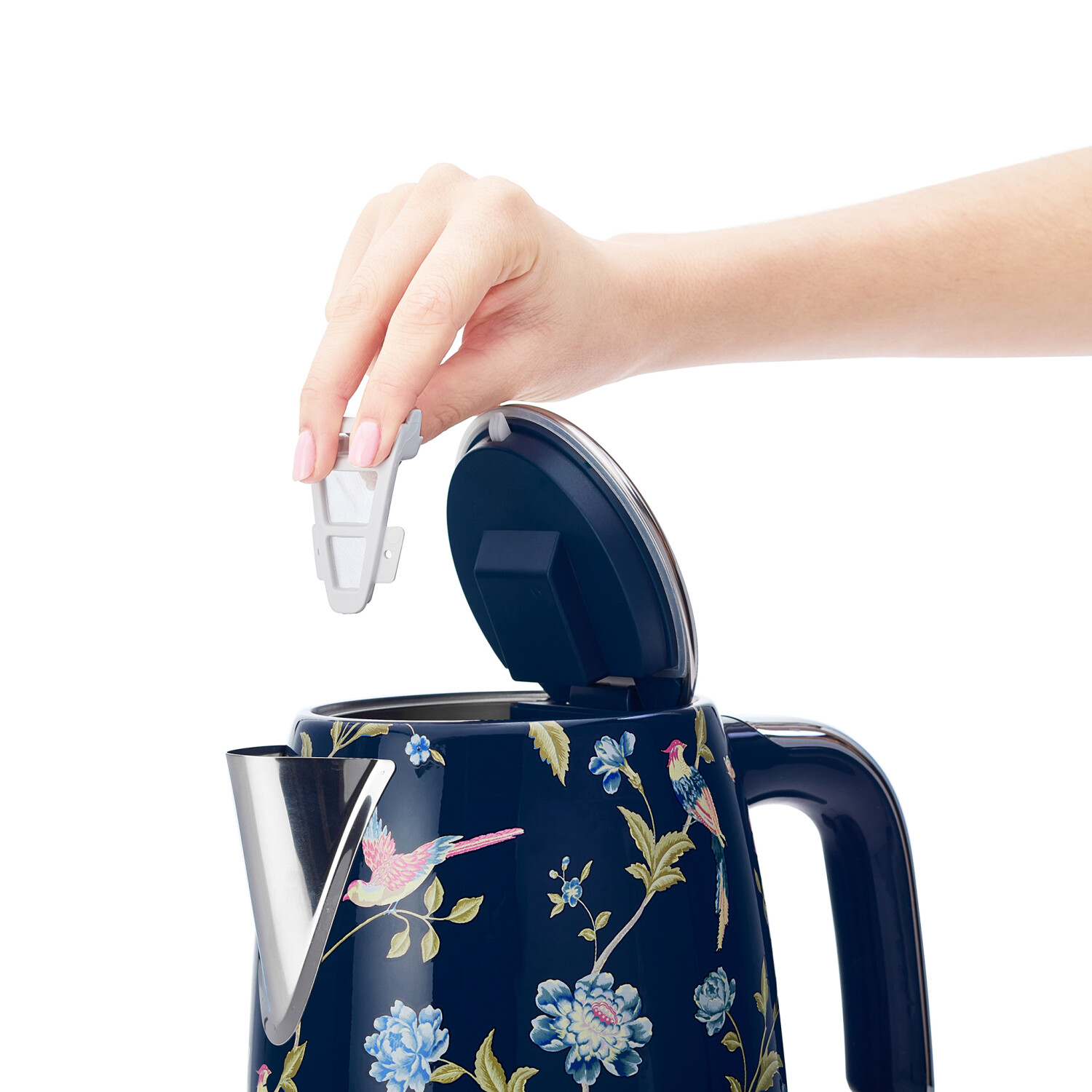Eine Hand legt einen Filter in einen blau blumig gemusterten Wasserkocher. Der Wasserkocher hat ein Vogeldesign und einen offenen Deckel. Weißer Hintergrund.