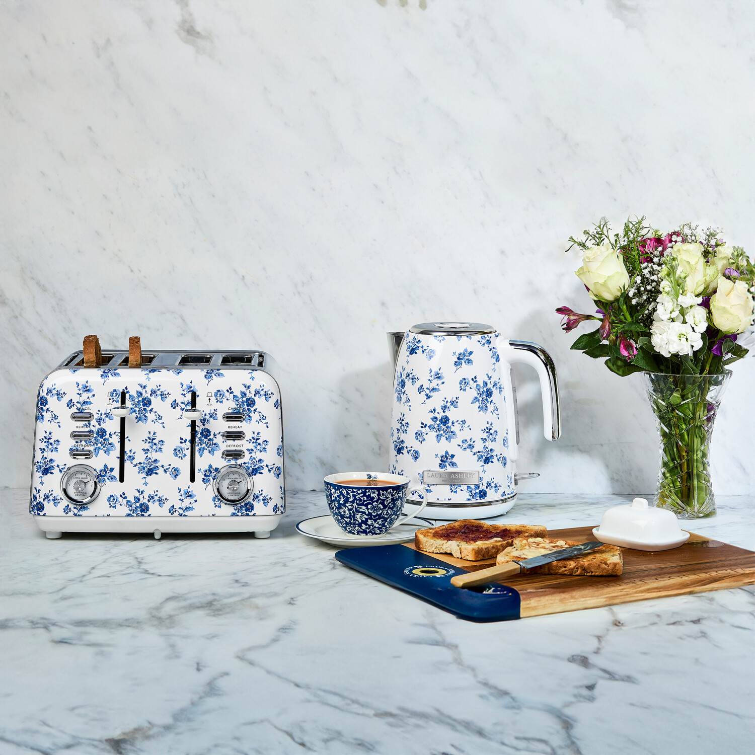 Küchenszene mit floralem Toaster, Wasserkocher, Tasse, Toast und Blumen auf Marmor.