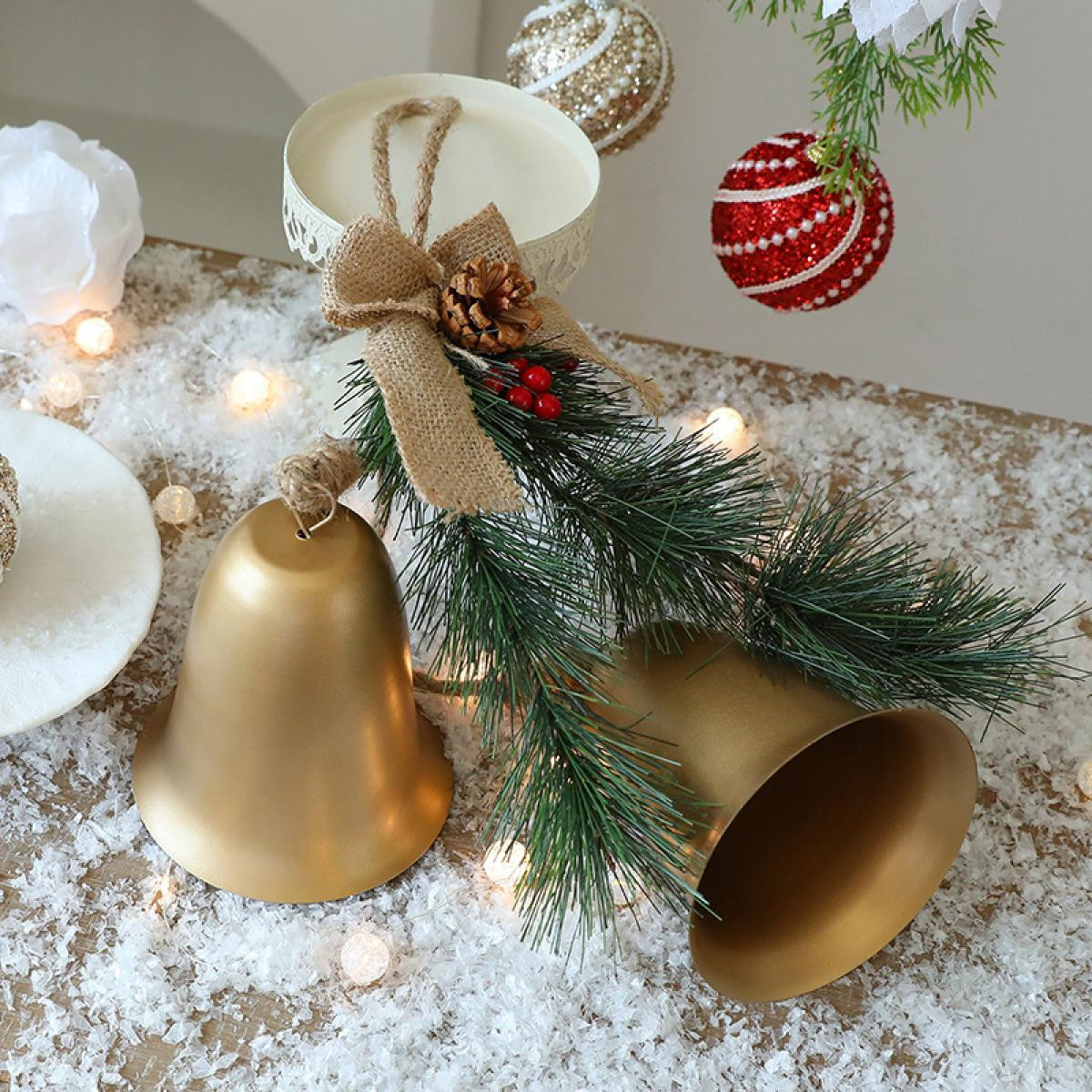 Goldene Glocken, Tannennadeln und Weihnachtsschmuck auf einer schneebedeckten Oberfläche. Eine Schleife und ein Tannenzapfen ergänzen die festliche Szene.
