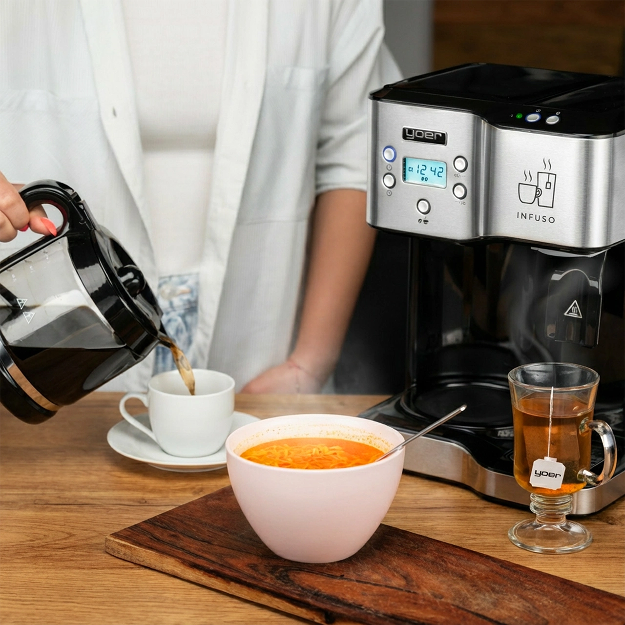 Osoba nalewa kawę do filiżanki, obok miski z zupą, szklanki herbaty i ekspresu do kawy.