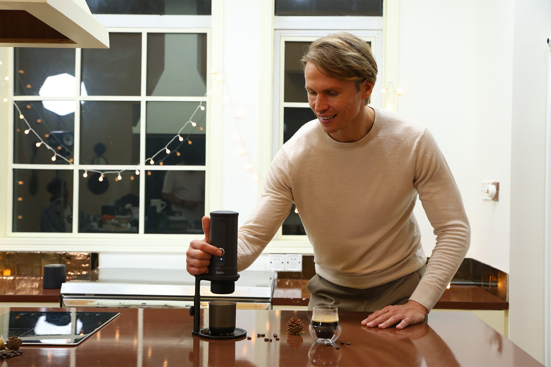 Mężczyzna w kuchni robi kawę. Trzyma ekspres do kawy, a obok niego stoi filiżanka kawy.
