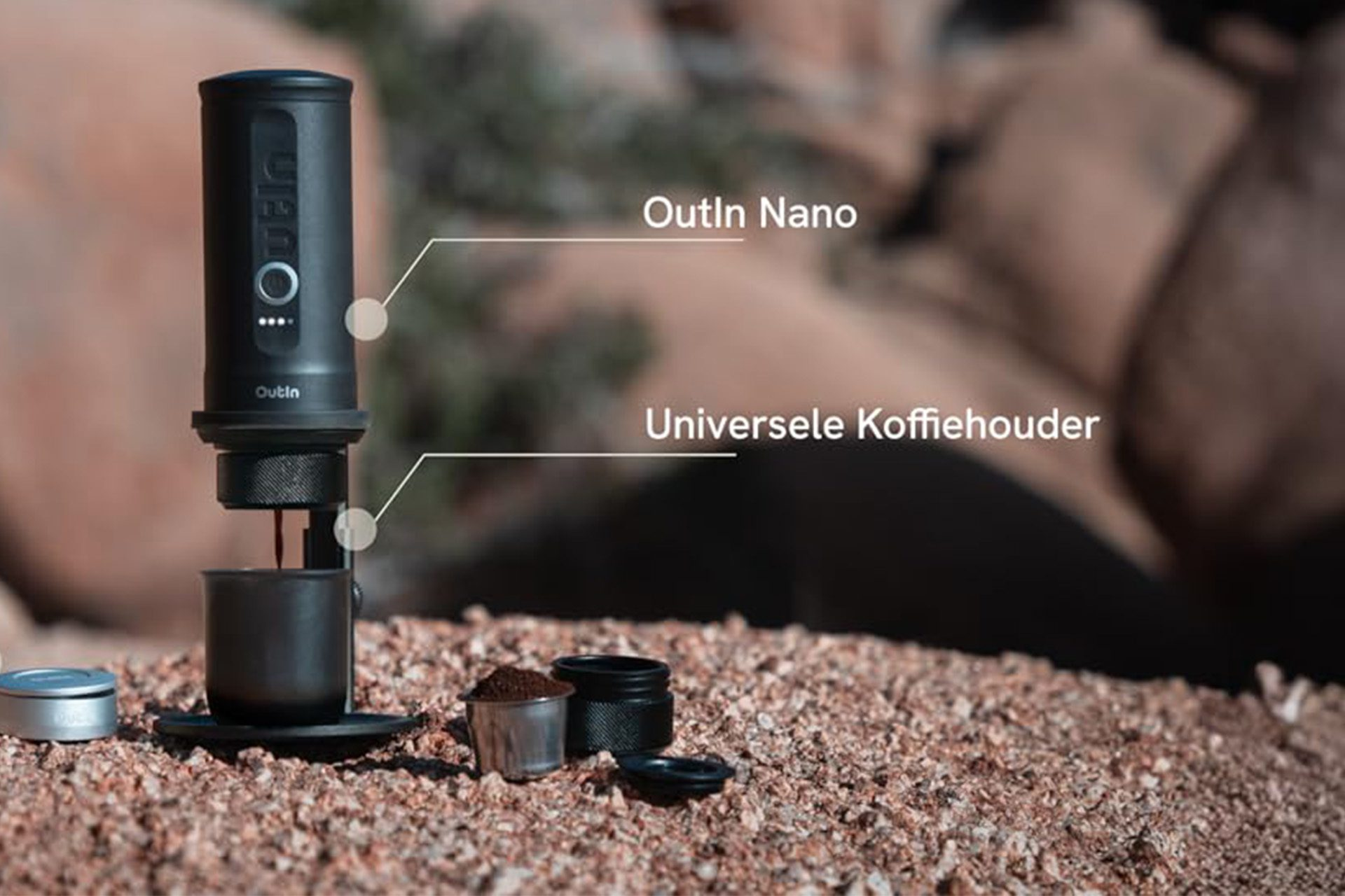 Czarny ekspres do kawy Outin Nano stoi na skalistej powierzchni. Kawa kapie do filiżanki. Obok zmielona kawa i akcesoria.