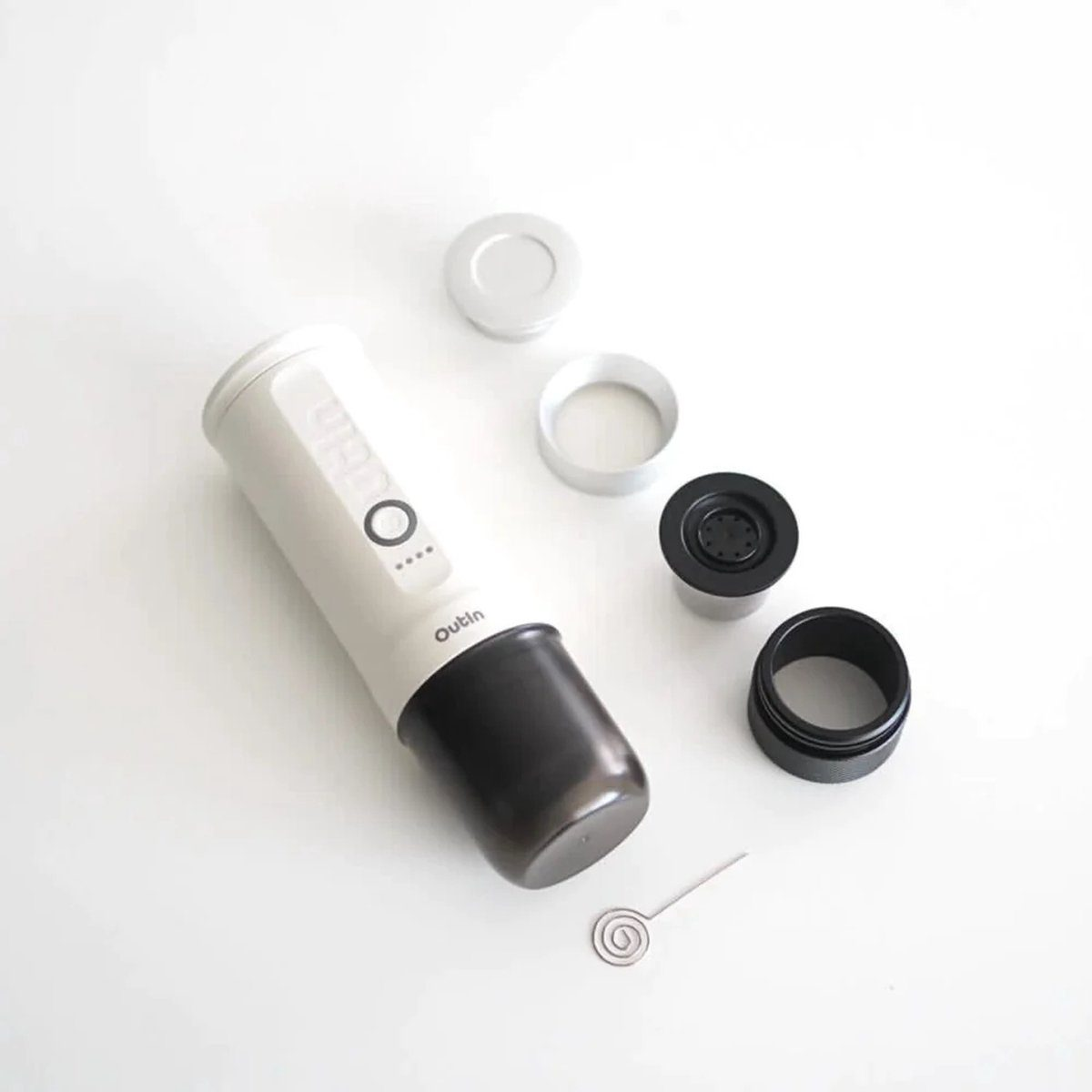 Ekspres do espresso zdemontowany na białej powierzchni. Części obejmują biało-czarny korpus, srebrne pierścienie i małą trzepaczkę.