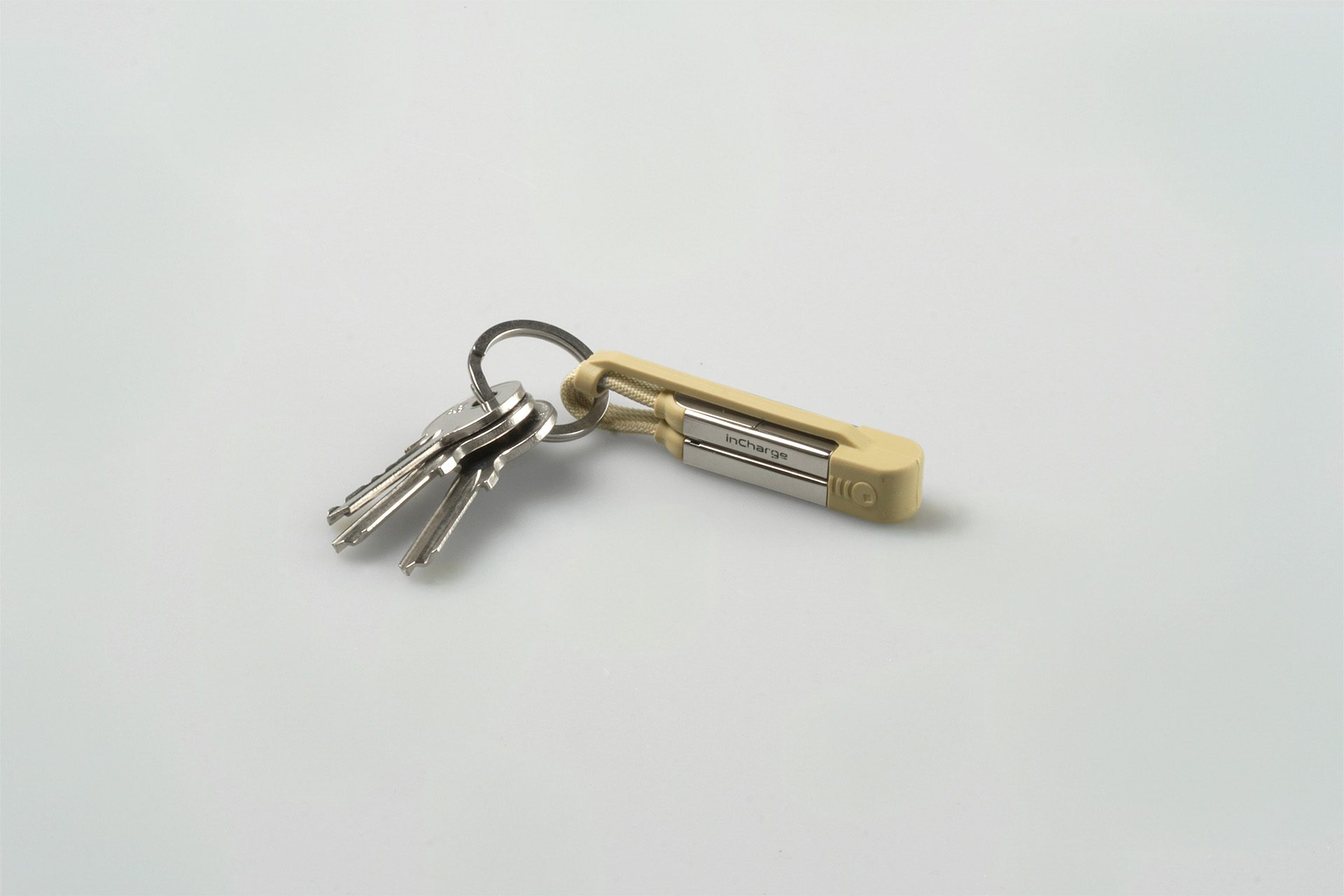 Sleutels en een beige Incharge-oplader op een wit oppervlak. De sleutels zijn zilverkleurig en de oplader heeft het Incharge-logo.