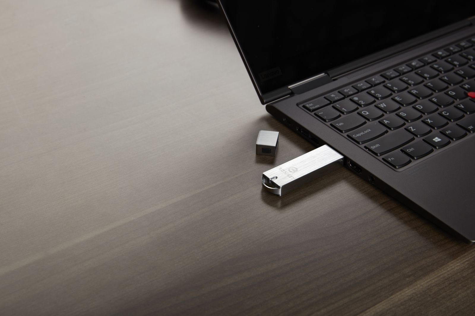 Laptop z włożonym pendrivem. Mała metalowa kostka leży obok na drewnianej powierzchni.