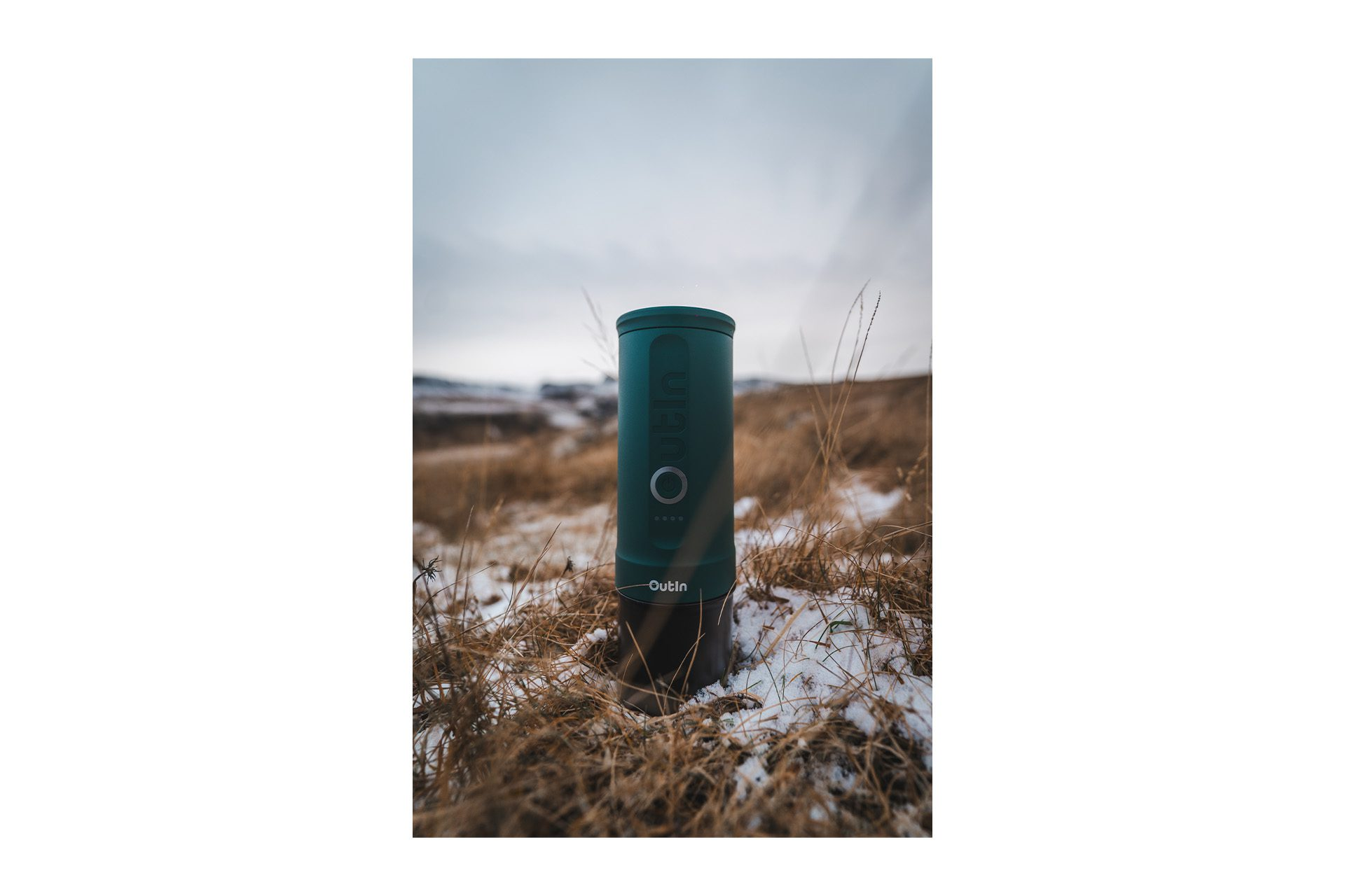 Zielone urządzenie Outin na polu suchej trawy i śniegu. Pochmurne niebo w tle.