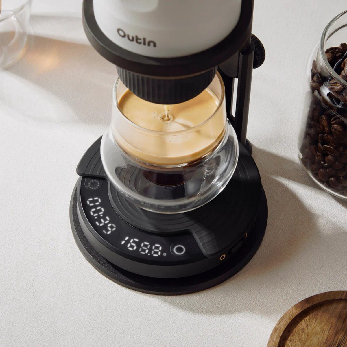 A coffee maker brewing coffee into a glass. A jar of coffee beans sits beside it. The maker has a digital display.