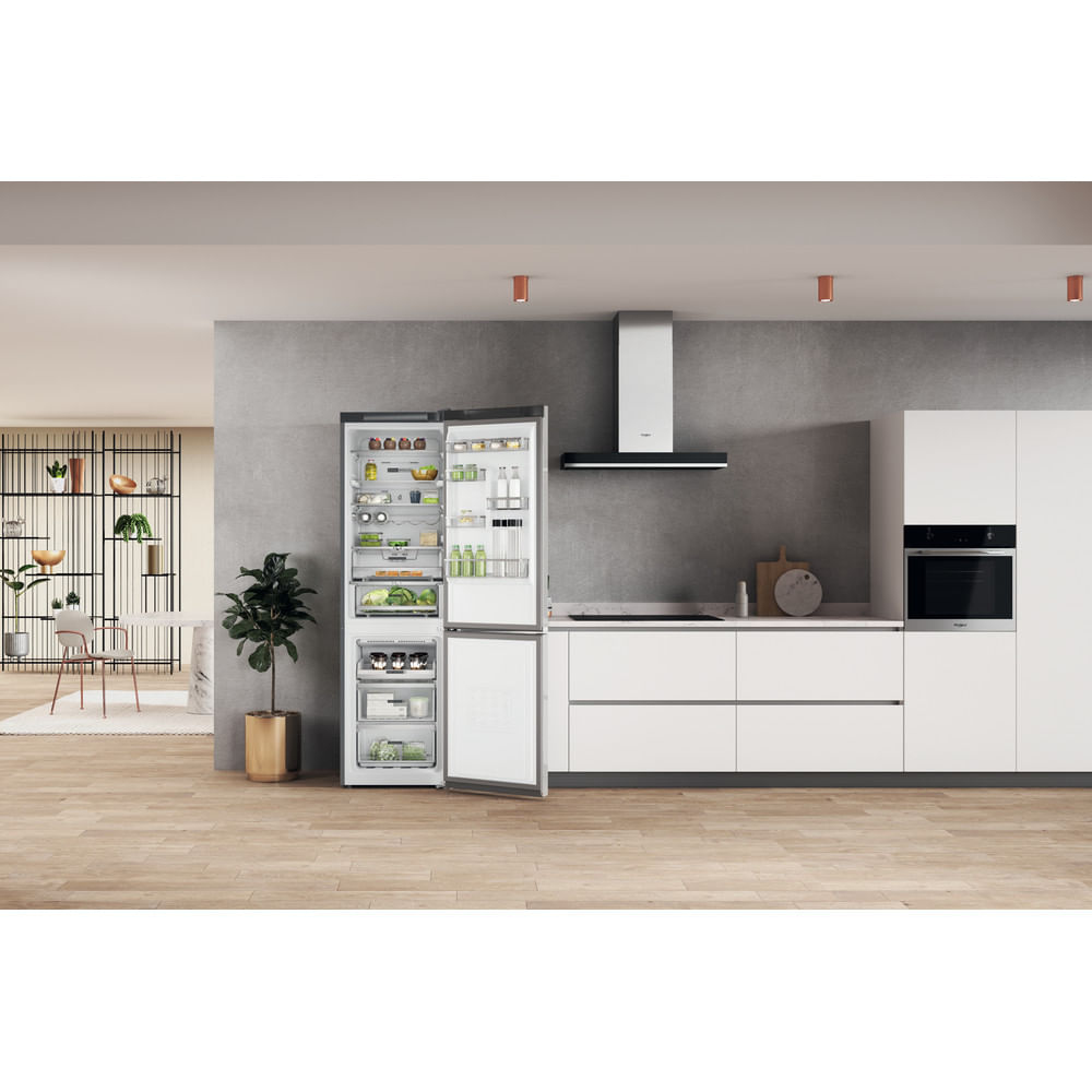 Cocina moderna con nevera abierta que muestra comida. Armarios blancos, campana extractora, planta y suelos de madera.