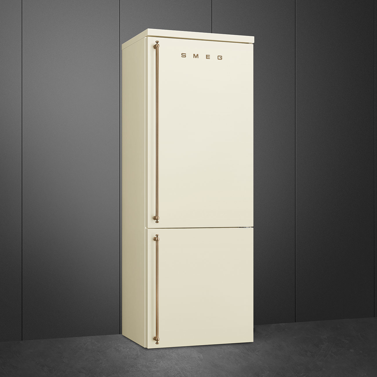 Un refrigerador SMEG crema se encuentra contra una pared de paneles gris oscuro. Tiene dos puertas con manijas de bronce.