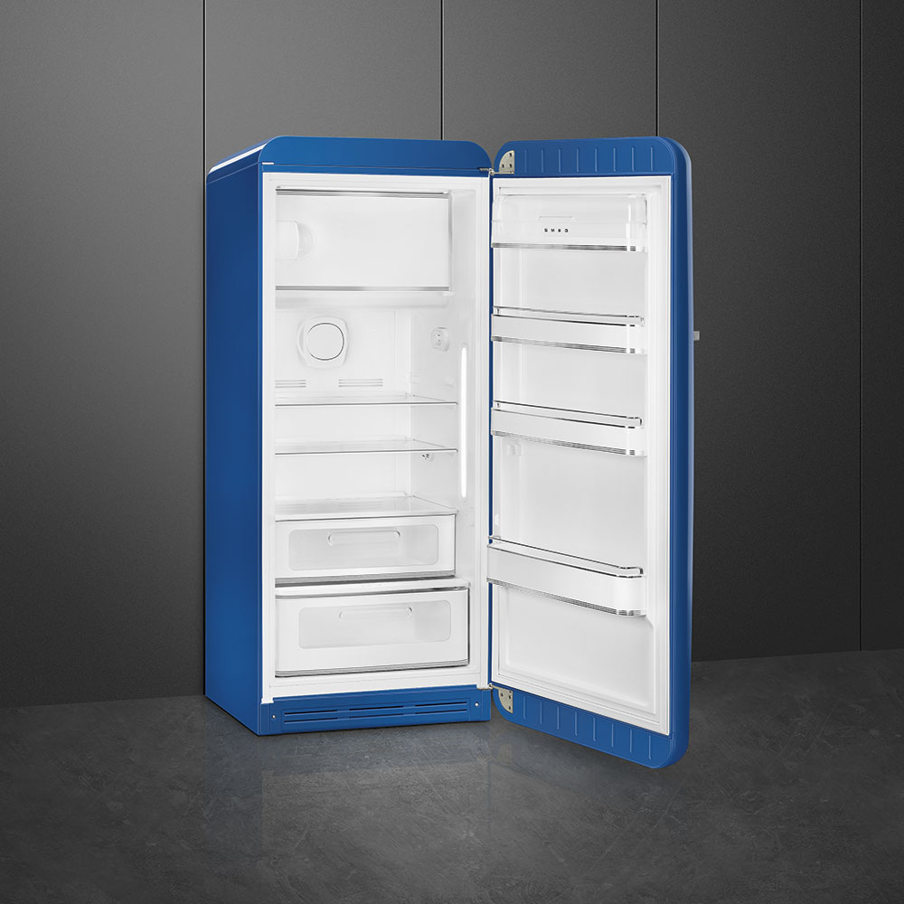 Un refrigerador Smeg azul, con la puerta abierta. En el interior, se ven estantes y cajones. El fondo es una pared y un suelo grises oscuros.