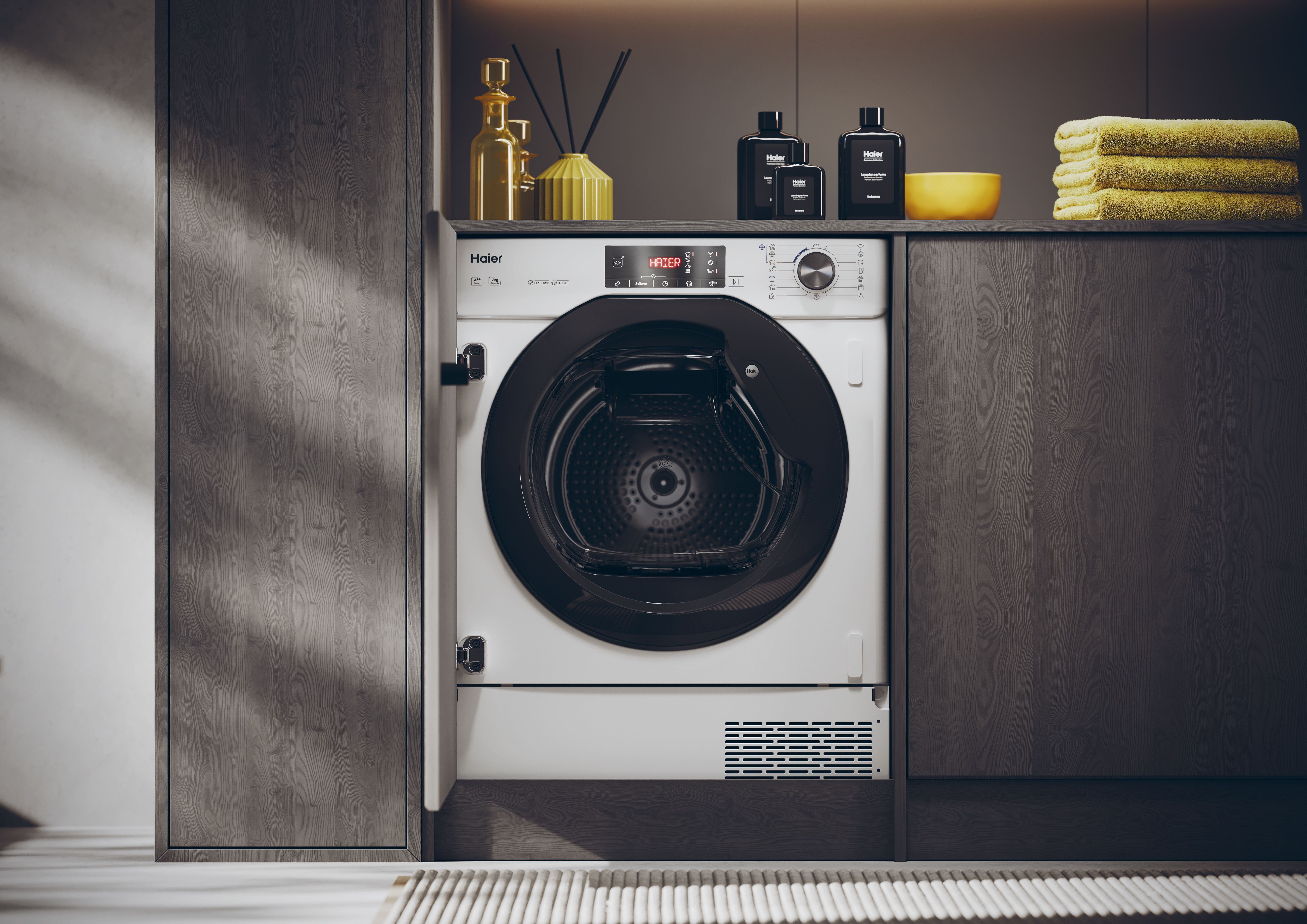 Biała suszarka Haier jest wyśrodkowana. Powyżej czarne butelki i żółta miska. Żółte ręczniki po prawej.