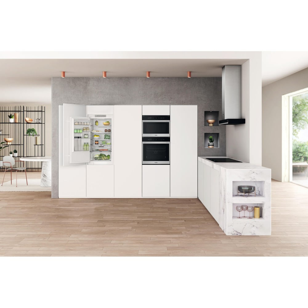 Cocina moderna con armarios blancos, nevera abierta, hornos e isla de encimera de mármol. Suelo de madera y ventana.