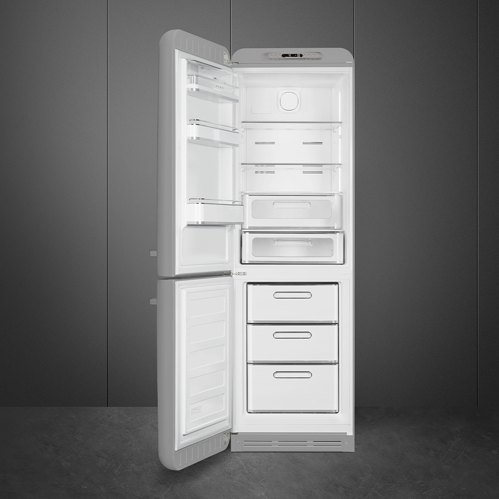 Un refrigerador blanco con la puerta abierta, mostrando estantes, cajones y compartimentos. El fondo es una pared gris oscura.
