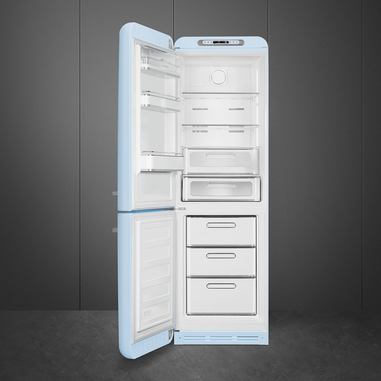 Un refrigerador retro azul claro está abierto, mostrando estantes y cajones. Se encuentra sobre un suelo oscuro contra una pared gris.