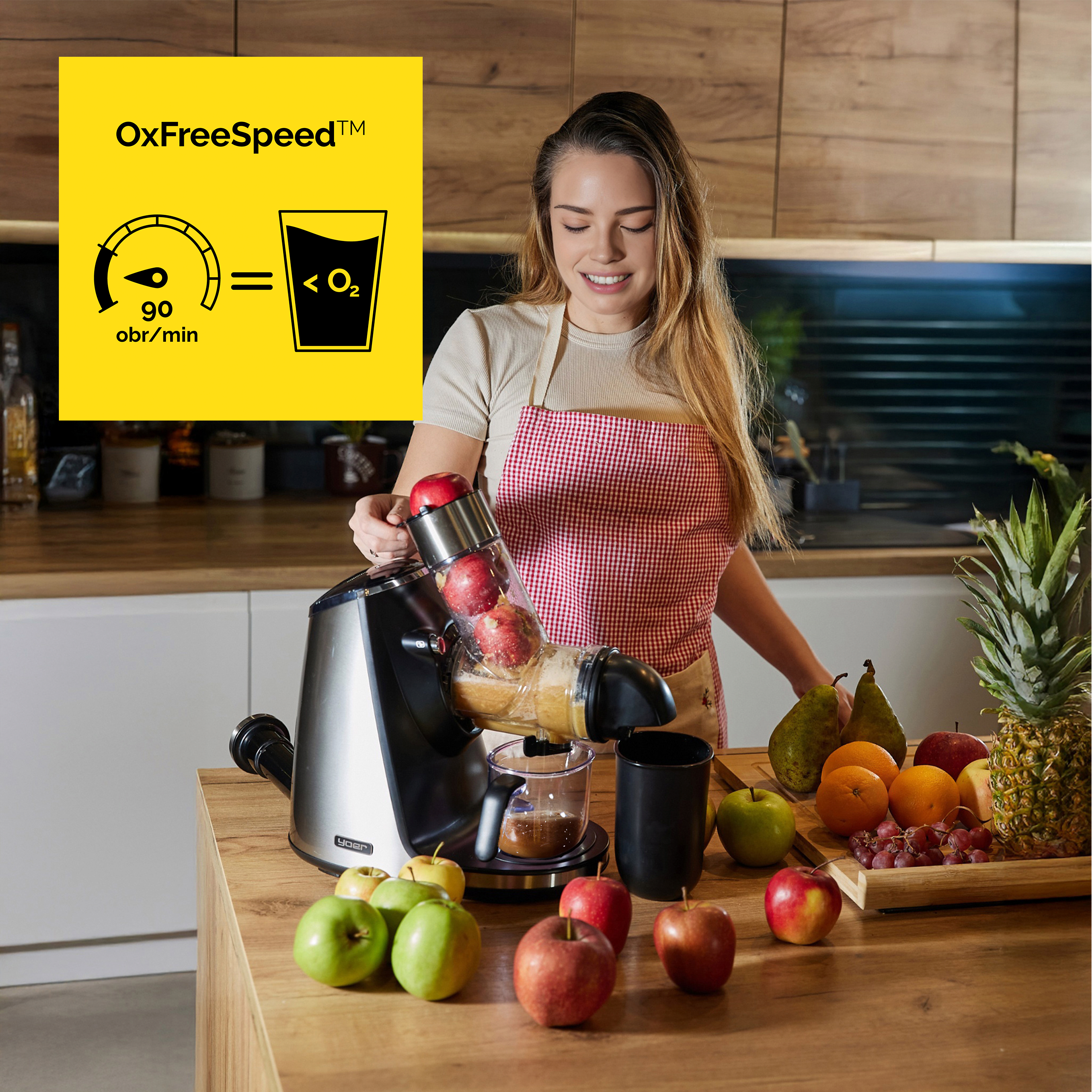 Kobieta wyciska sok z jabłek maszyną. Jabłka, pomarańcze, winogrona i ananas na stole.