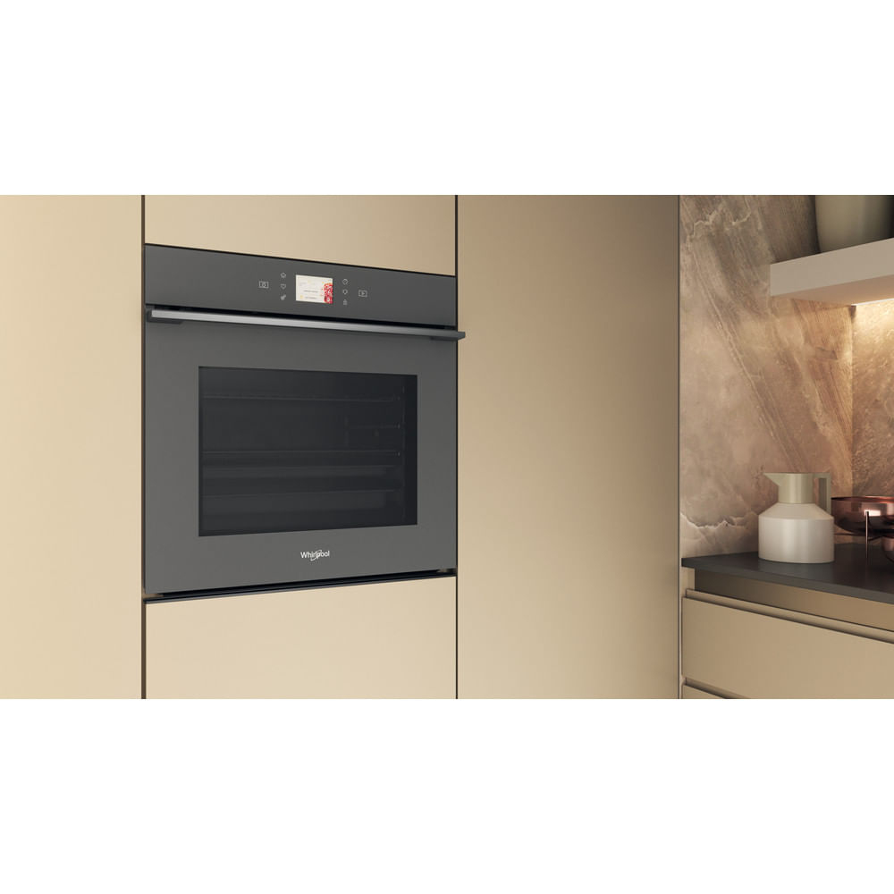 Una cucina moderna con forno Whirlpool integrato. Mobili beige circondano il forno, con piano di lavoro e brocca bianca a destra.