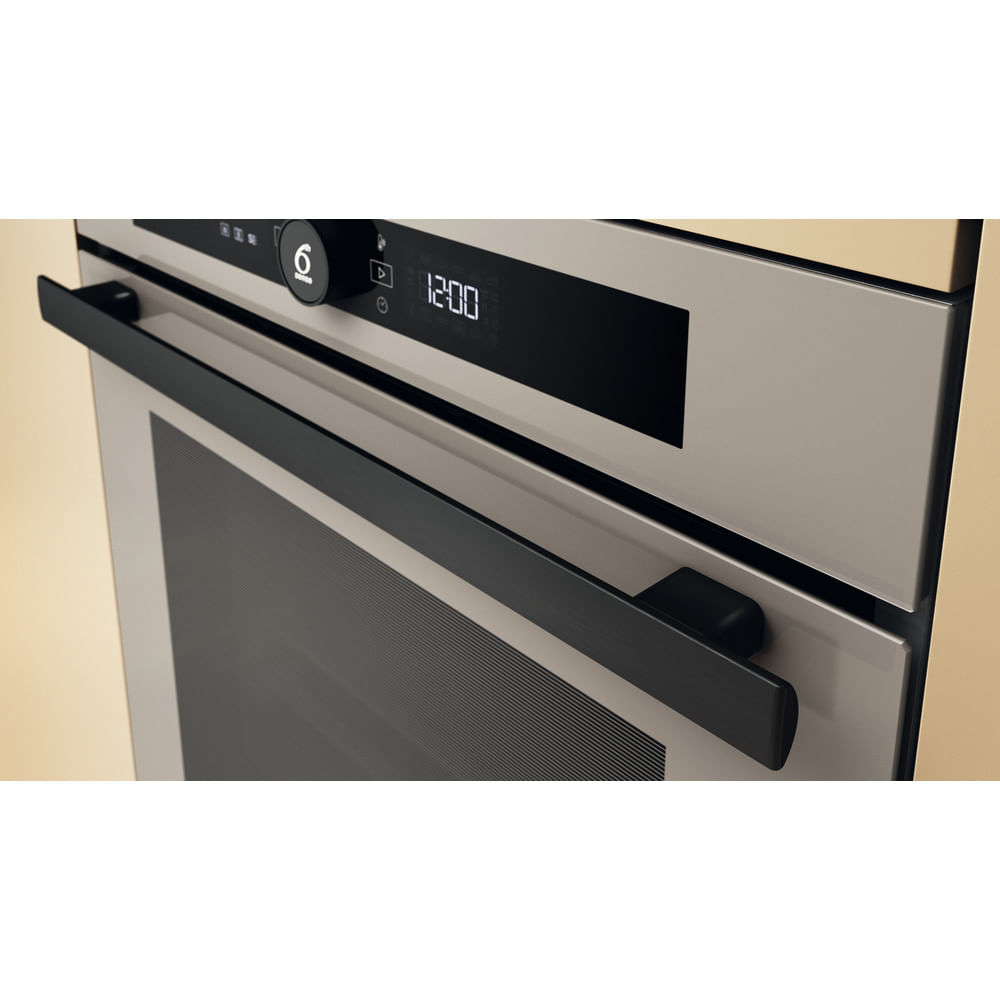 Primo piano di un forno moderno. Ha una maniglia nera, un display digitale che mostra le 12:00 e una superficie color argento. Lo sfondo è color crema.