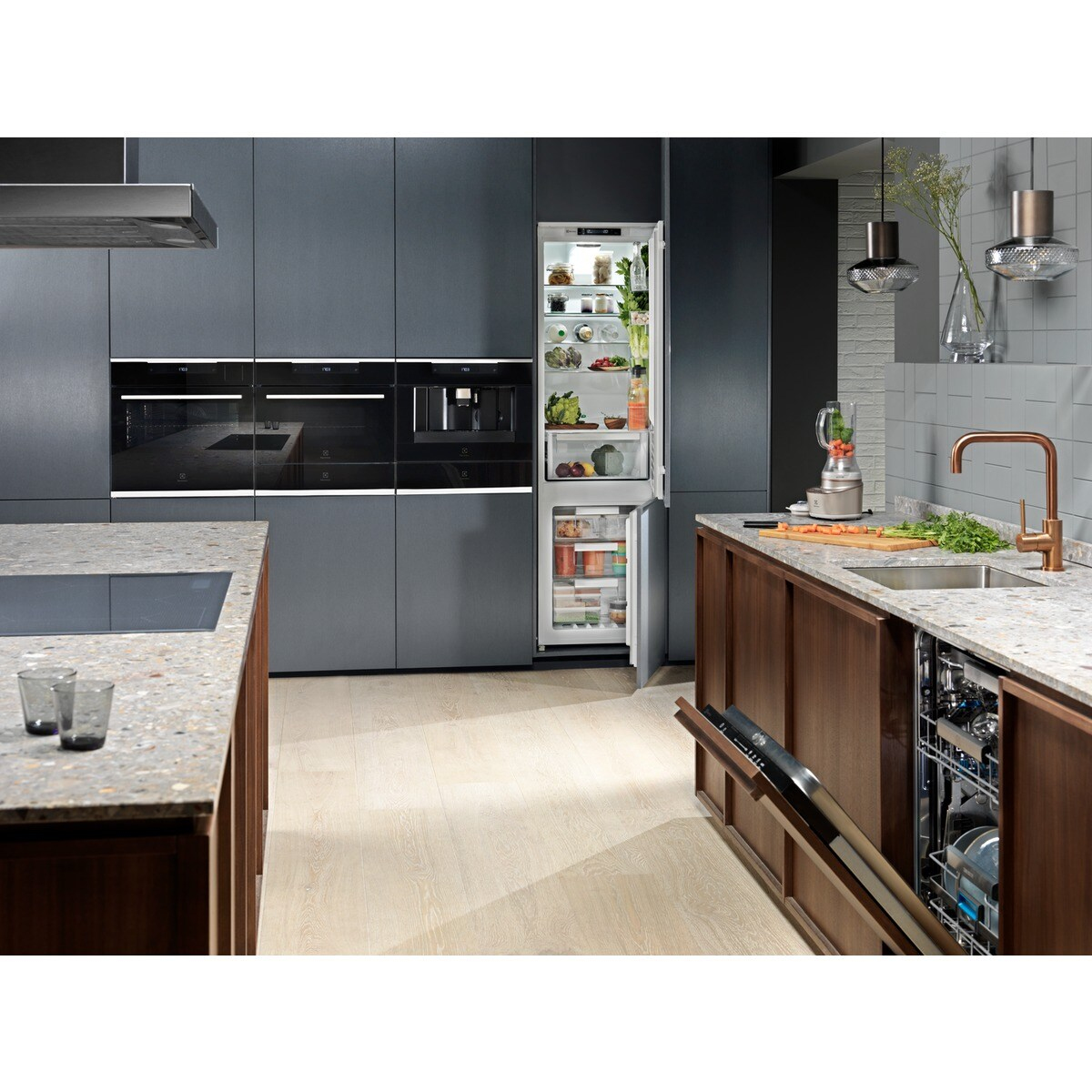 Cucina moderna con frigorifero aperto, elettrodomestici da incasso e mobili in legno. Frullatore e lavello visibili. Pavimento in legno chiaro.