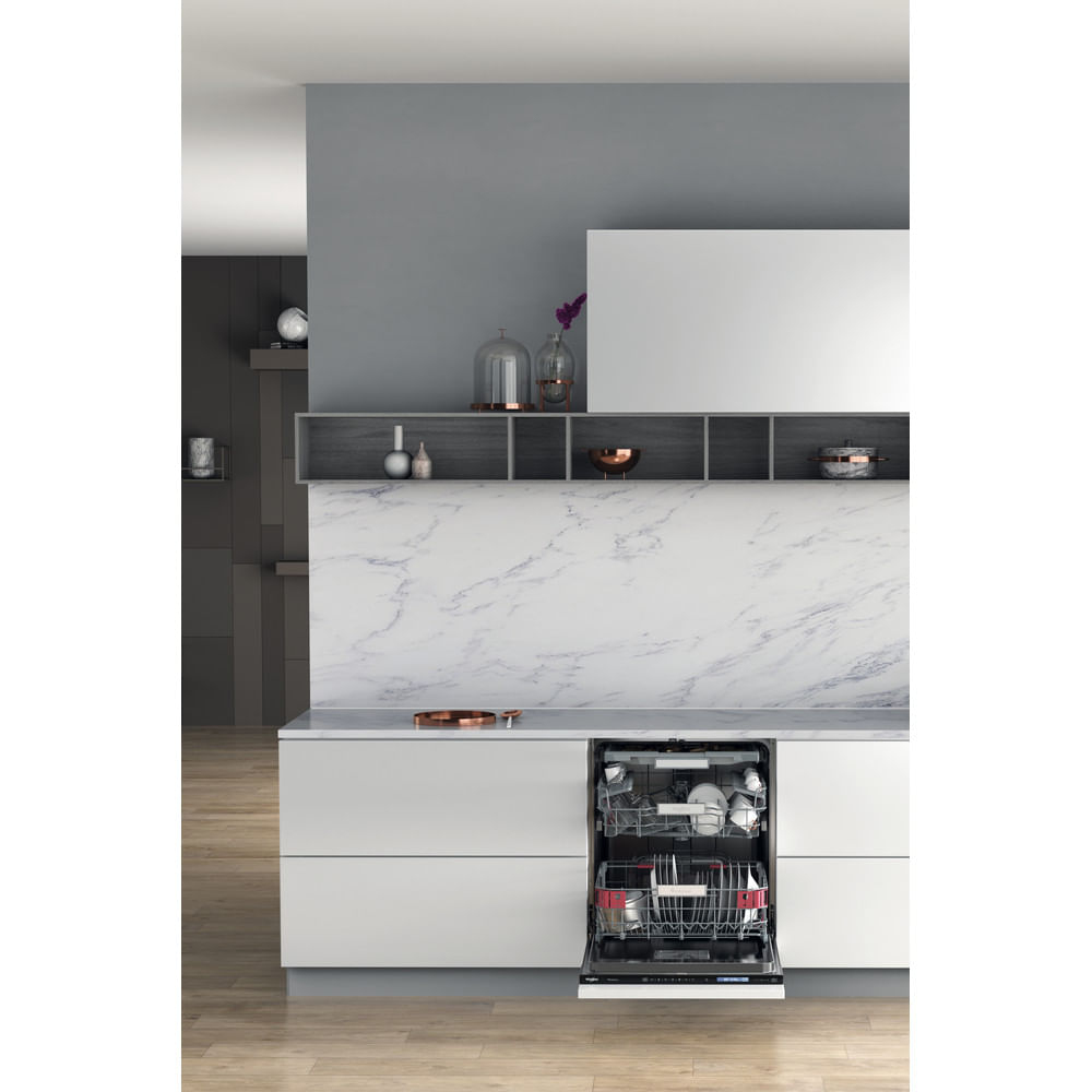 Cocina moderna con lavavajillas abierto. Platos dentro, armarios blancos, salpicadero mármol, pared gris y objetos decorativos en estante.