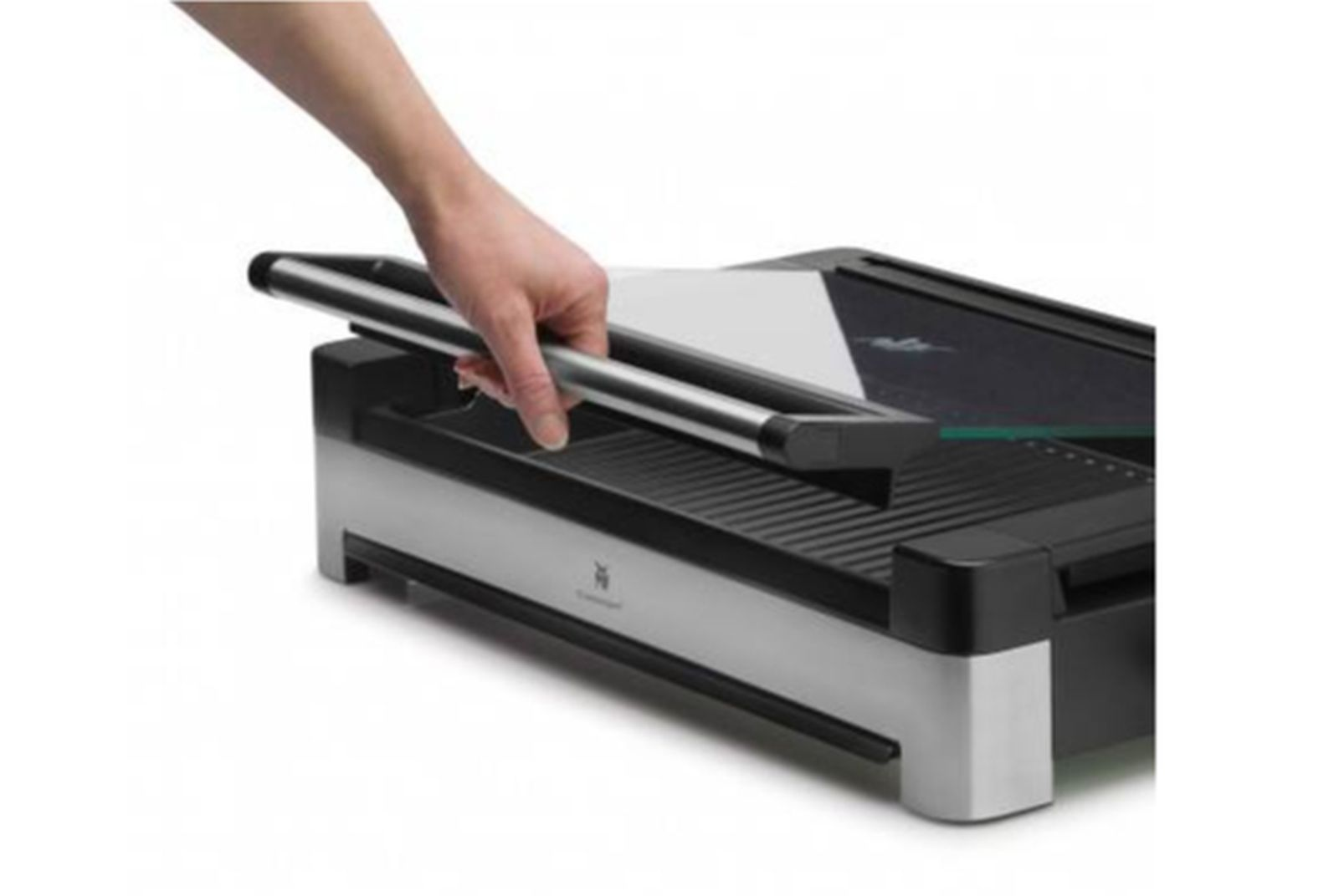 Ręka pociąga za dźwignię czarno-srebrnego urządzenia kuchennego. Wkładany jest biały papier.