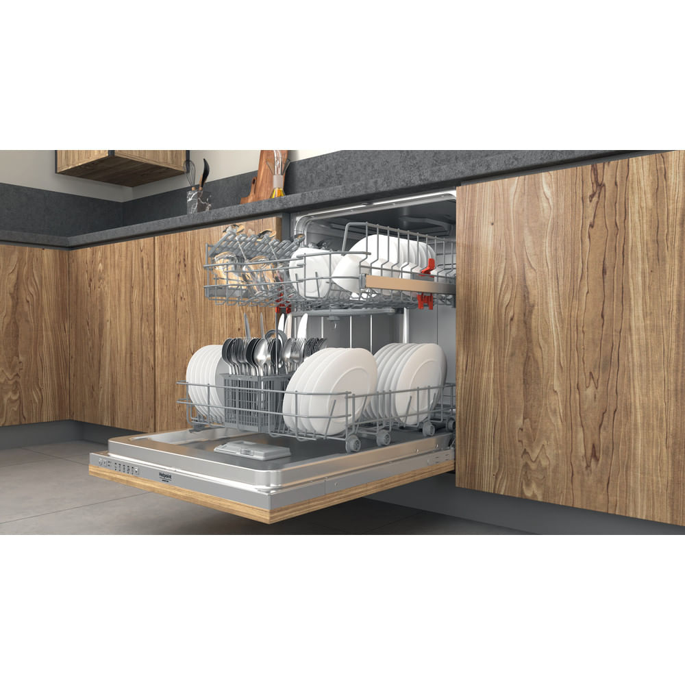 Lavavajillas abierto con platos y cubiertos dentro. Se ven gabinetes de madera y encimera. El lavavajillas está en un entorno de cocina.